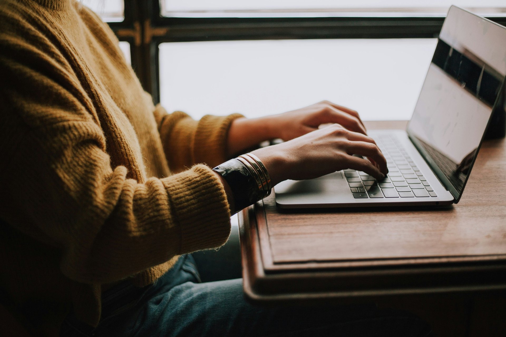 Photograph of a person sat at a desk with their hands on the keyboard of a laptop