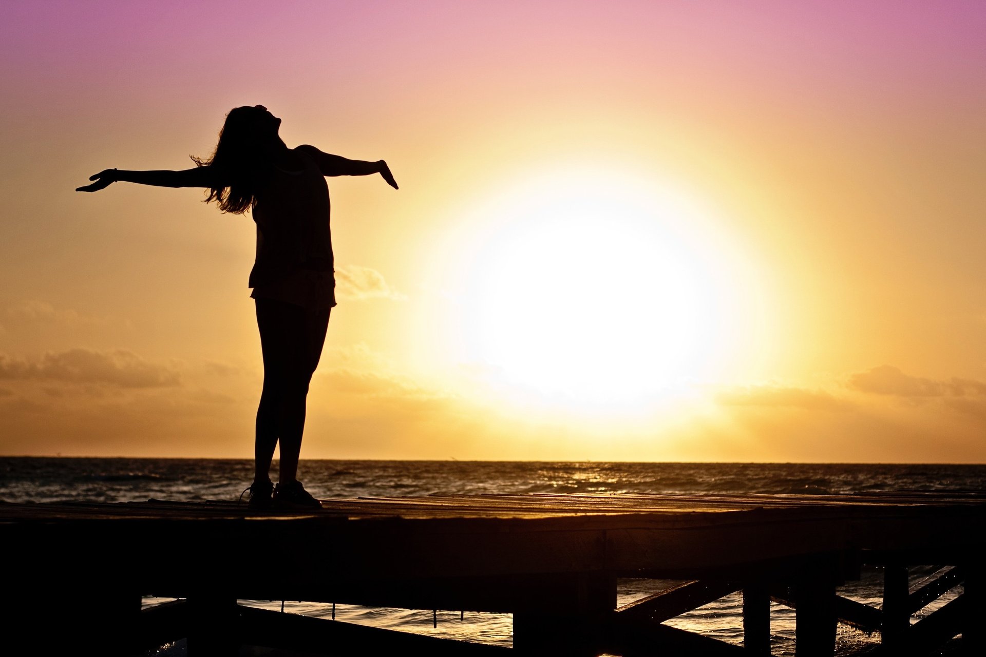 a woman standing on a dock with her arms outstretched out to the water