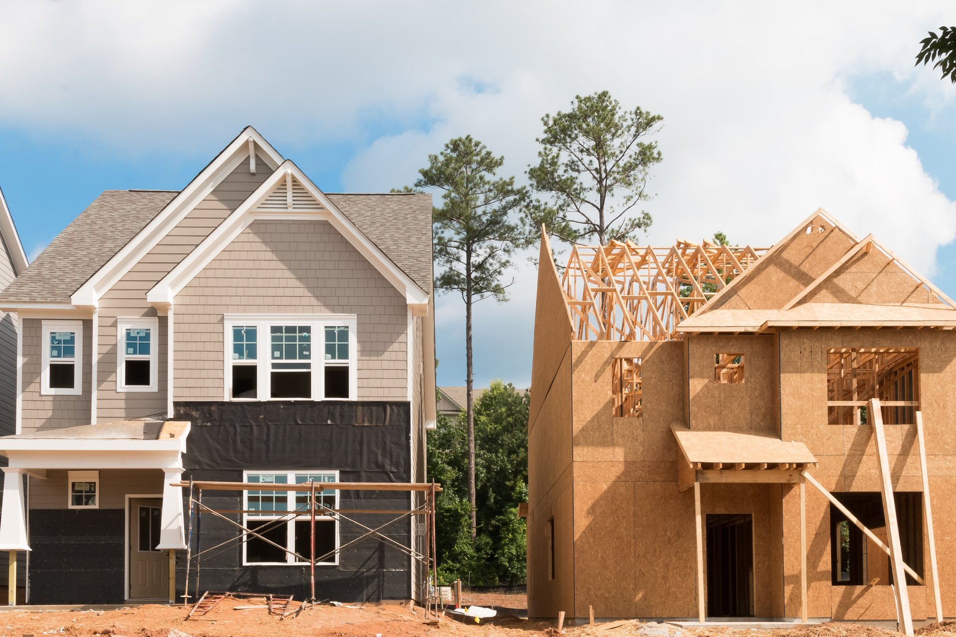 Two homes side by side showing different construction phases, from framing to near-complete exterior