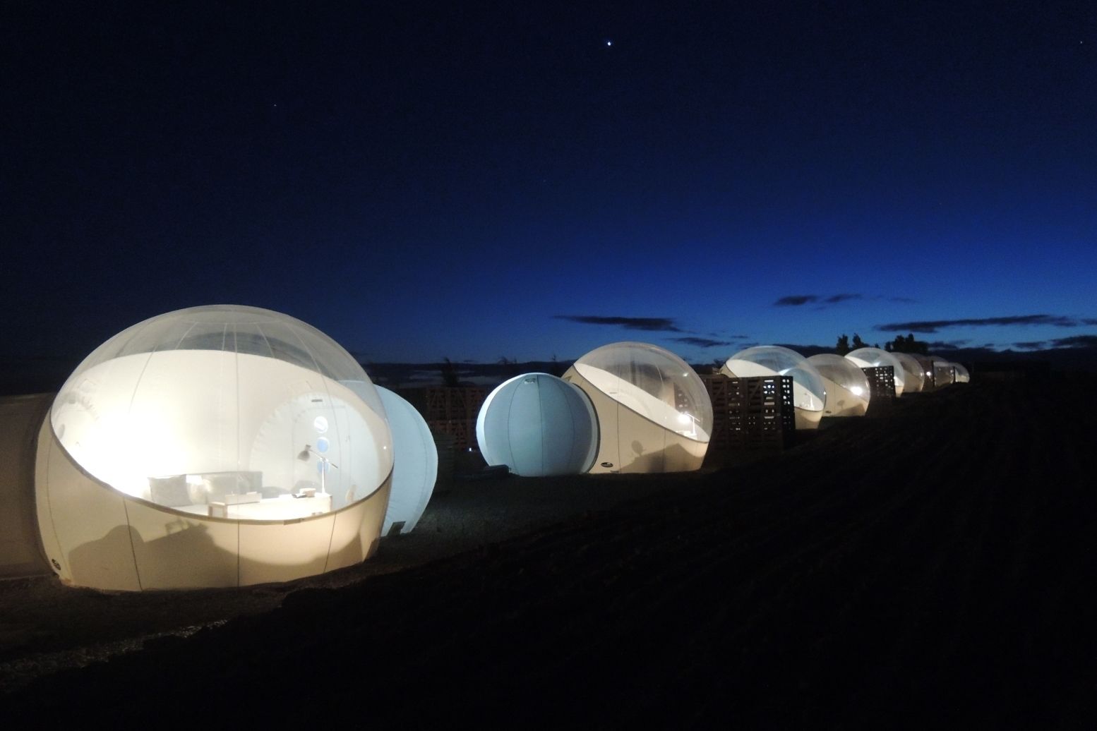 Illuminated luxury bubble hotel tents for glamping under a dark starry night sky.