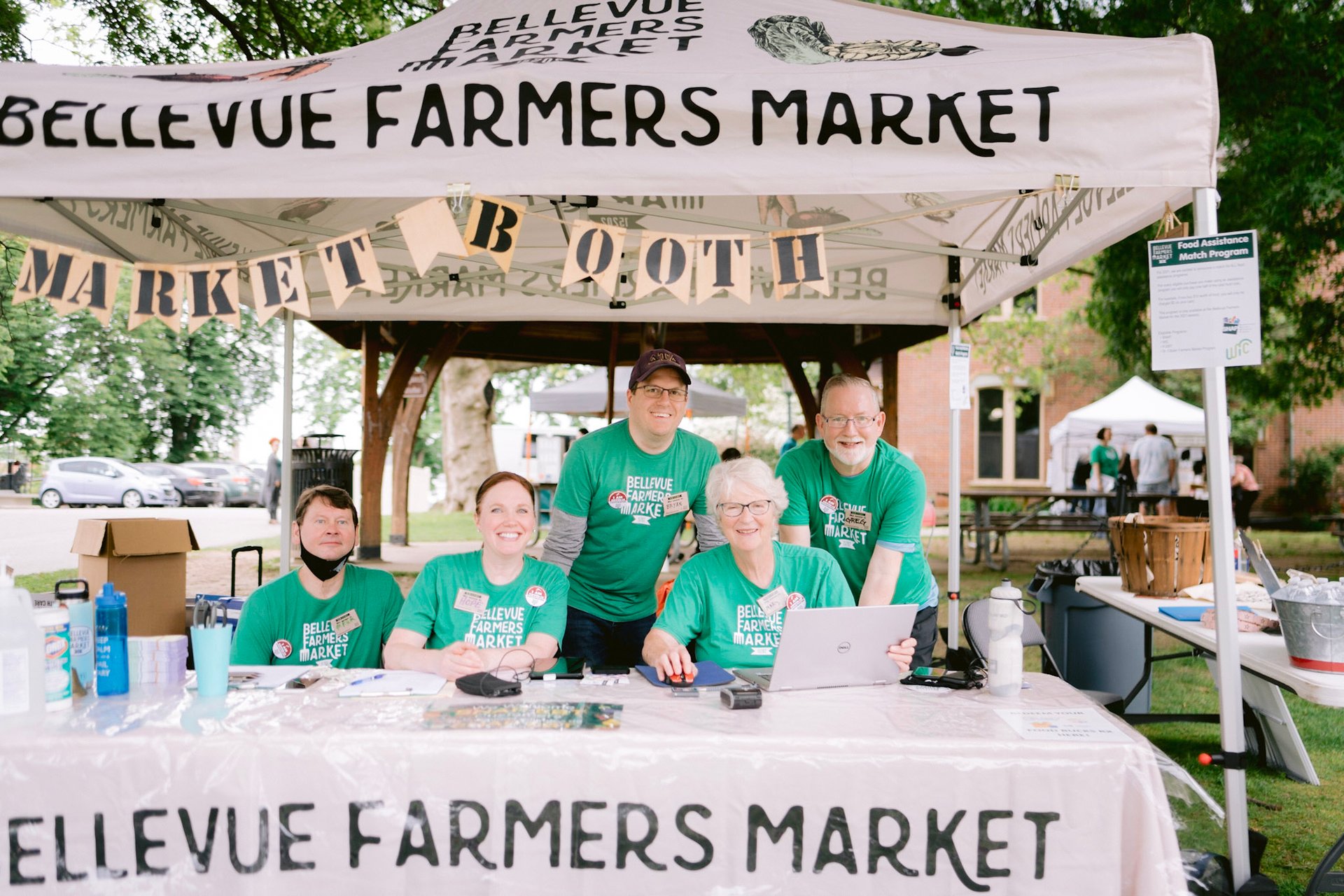 Volunteers smile from behind the Bellevue Farmers Market information booth.