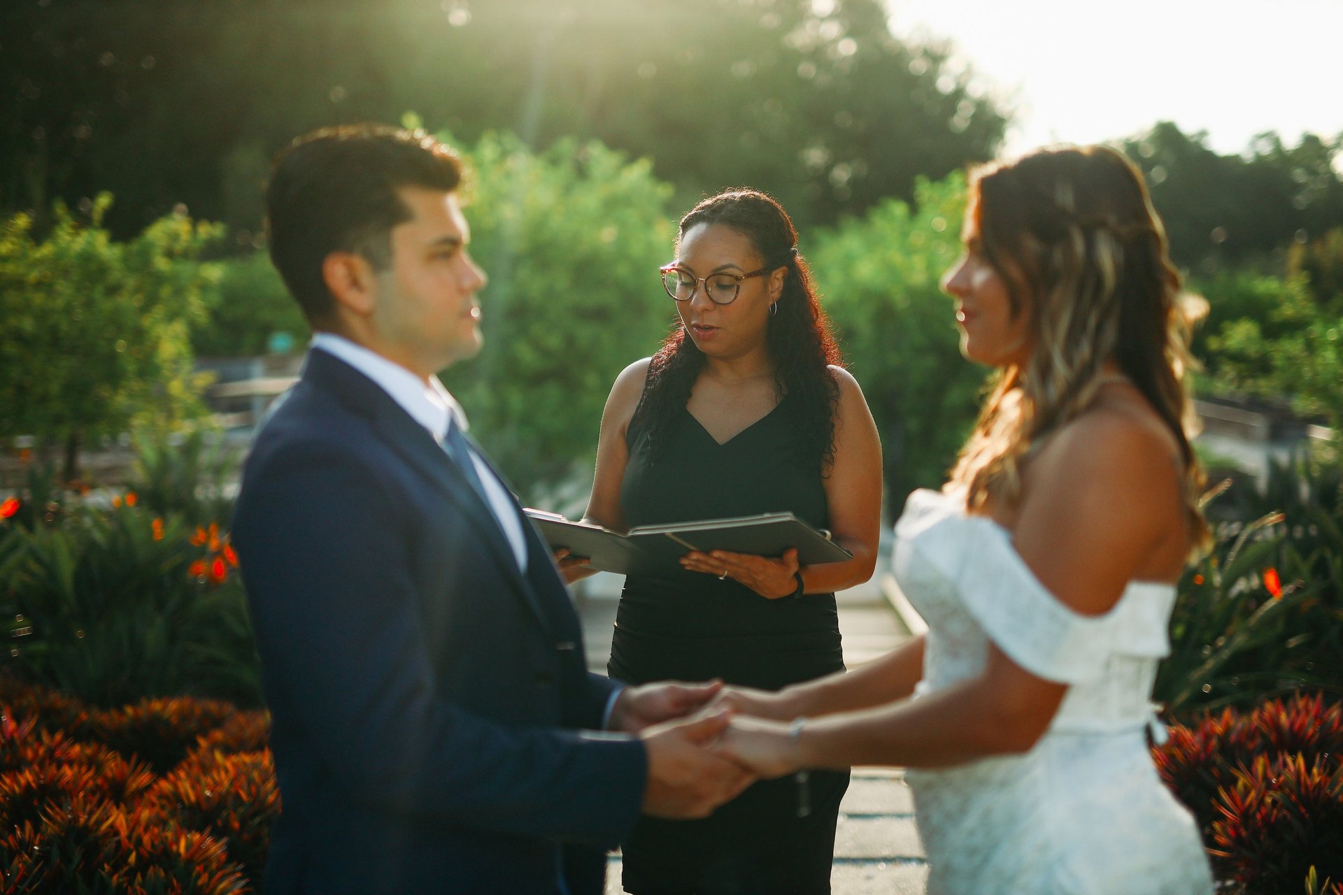Wedding officiant performing a garden ceremony for a bride and groom during golden hour.