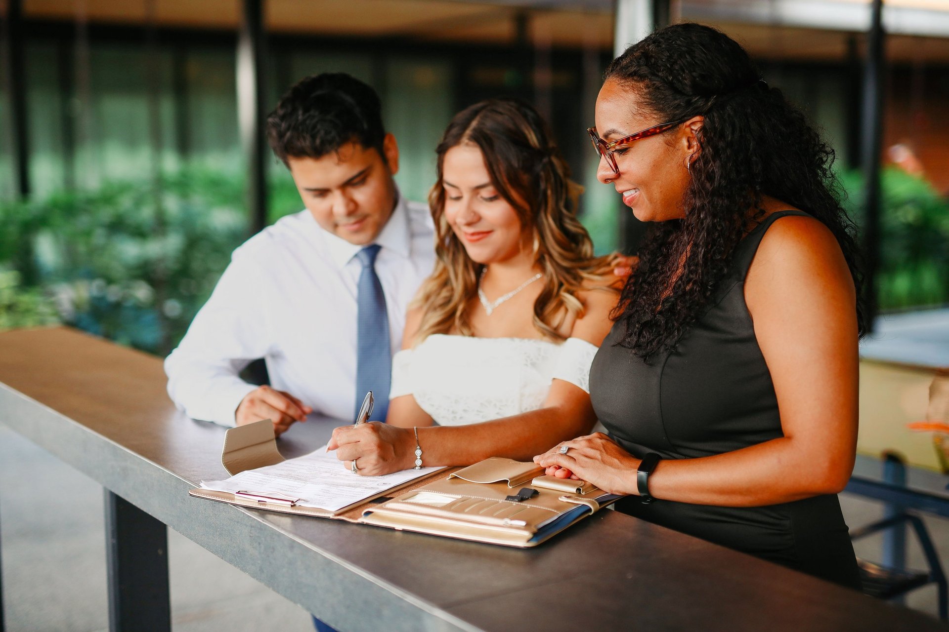 A bride and groom signing their marriage certificate with a wedding officiant at an outdoor ceremony.