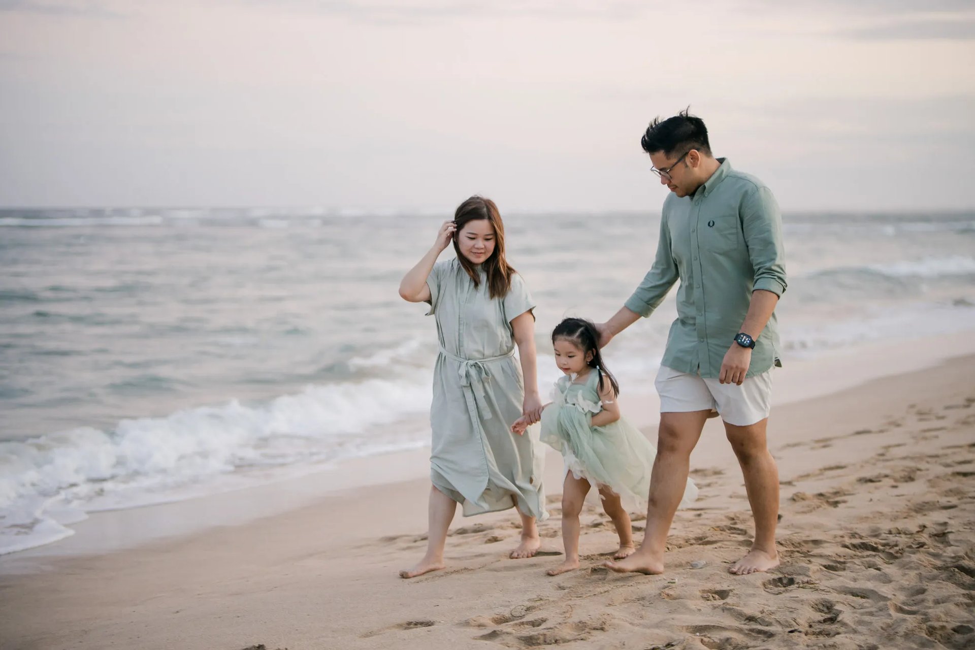 Parents and daughter walking together along the beach during a family photography session in Nusa Dua Bali.
