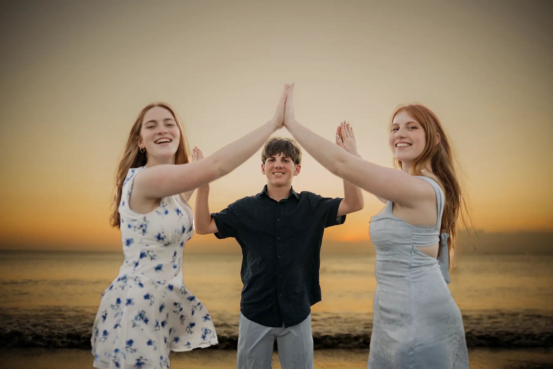 Family sharing a playful high-five during a sunset family photography session at Jimbaran Beach Bali