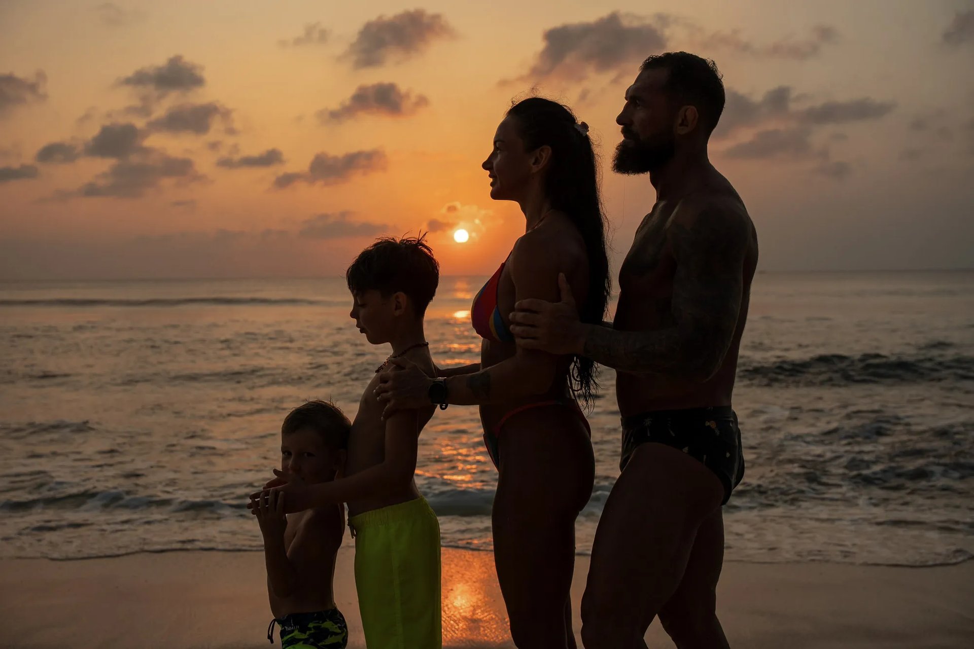 Family silhouette at sunset on Dreamland Beach Bali with parents holding their son during a golden hour family photography 