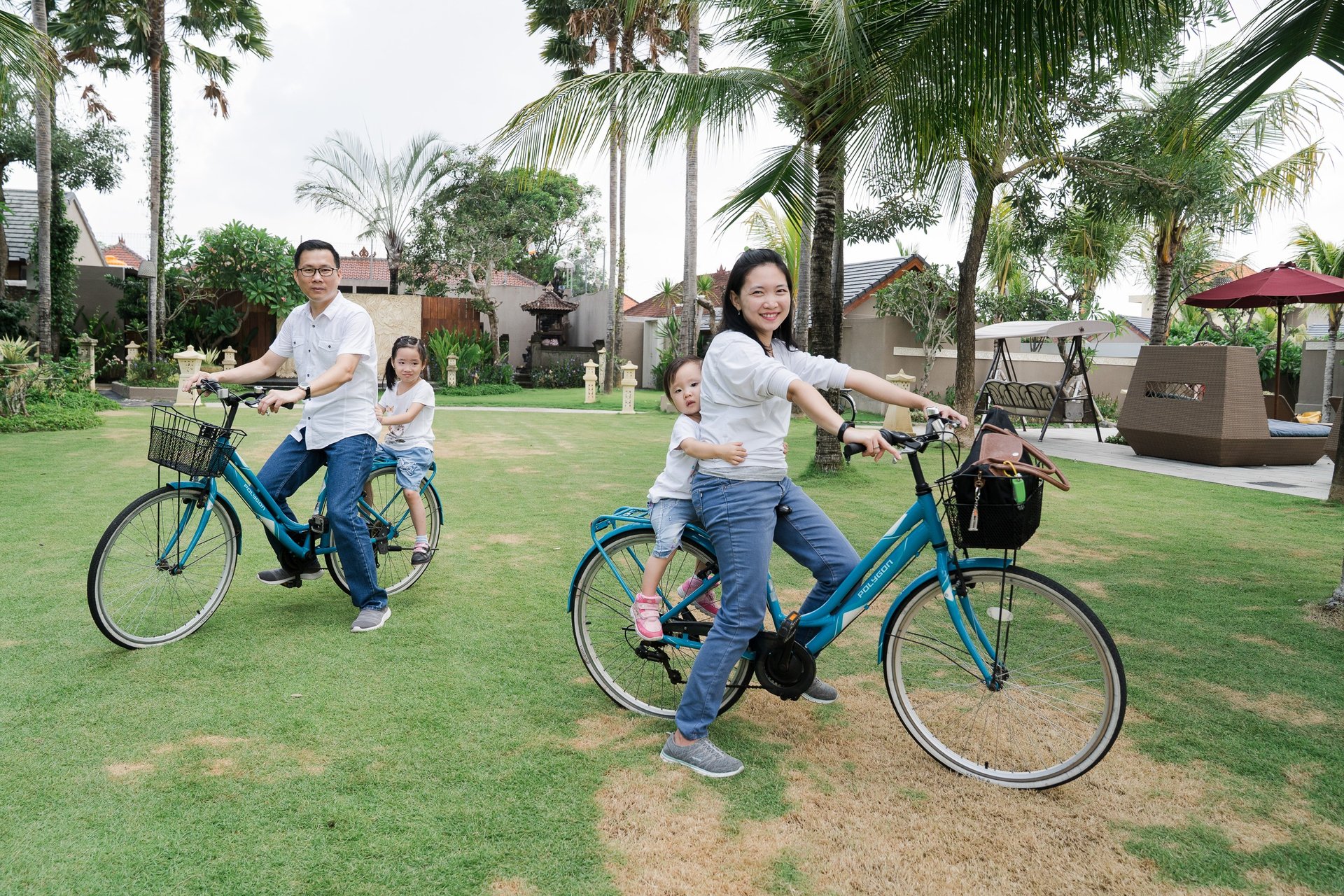 Family biking together during extended family photography session at Lumbini Villas Jimbaran Bali in a tropical garden