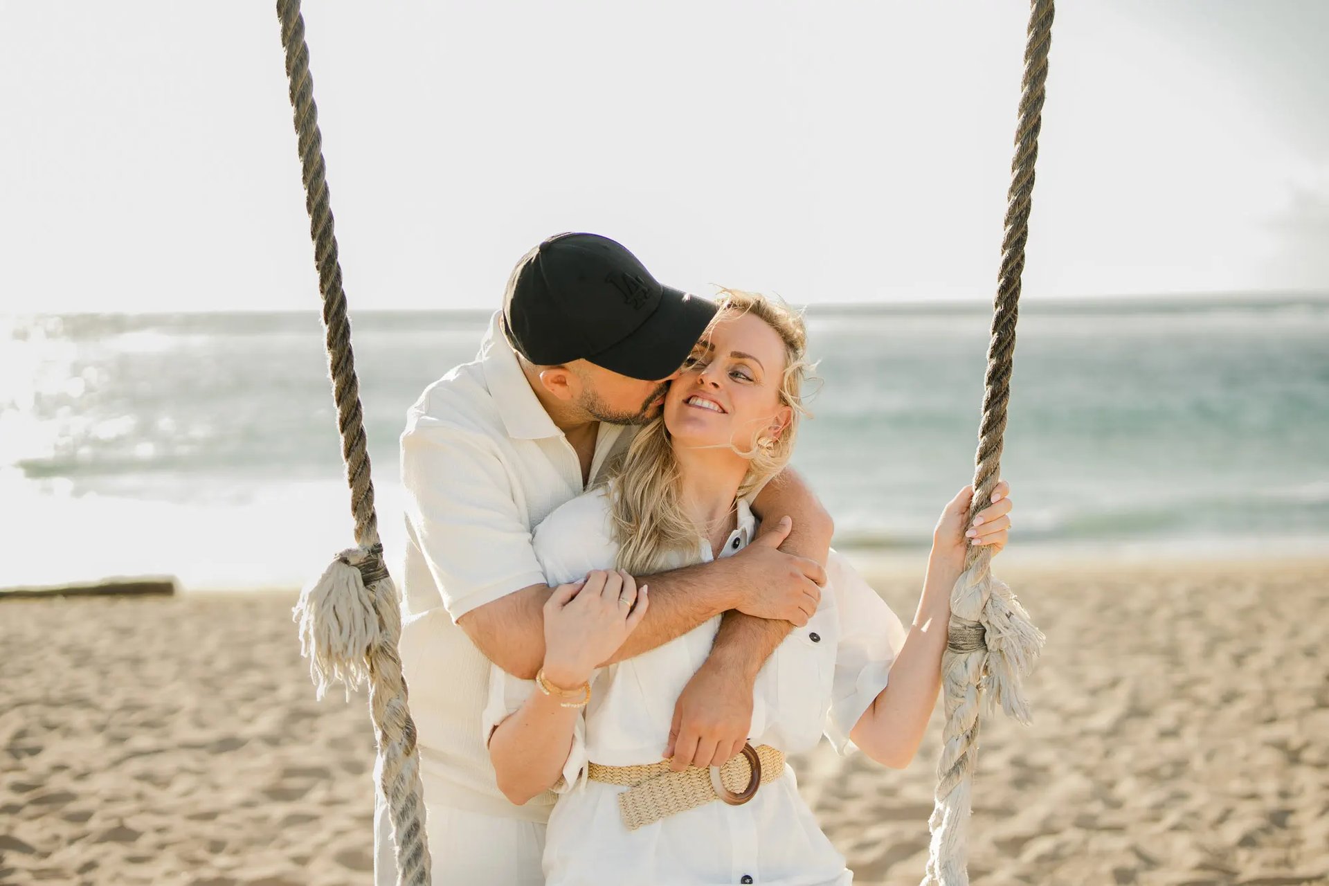 Mother and daughter sharing a loving embrace on a beach swing during a family photography session at Ayodya Resort Bali