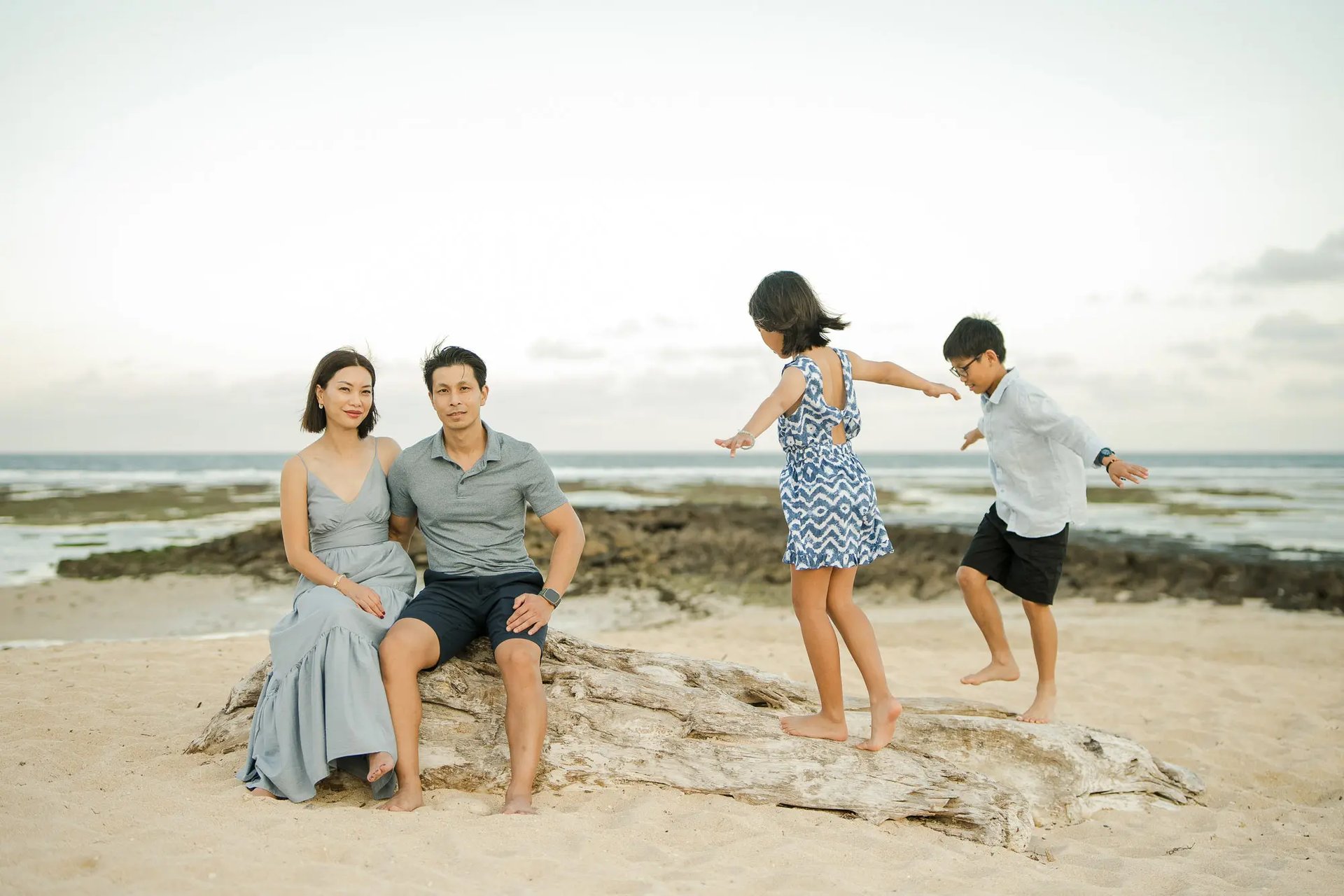 Family sharing playful moments on coastal rocks during a family photography session at The Ritz-Carlton Bali.