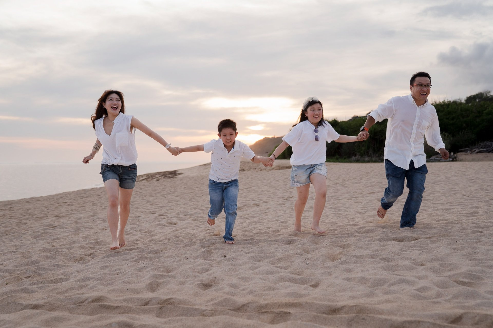 Family running together on the sandy beach during a sunset family photography session at The Ritz-Carlton Bali
