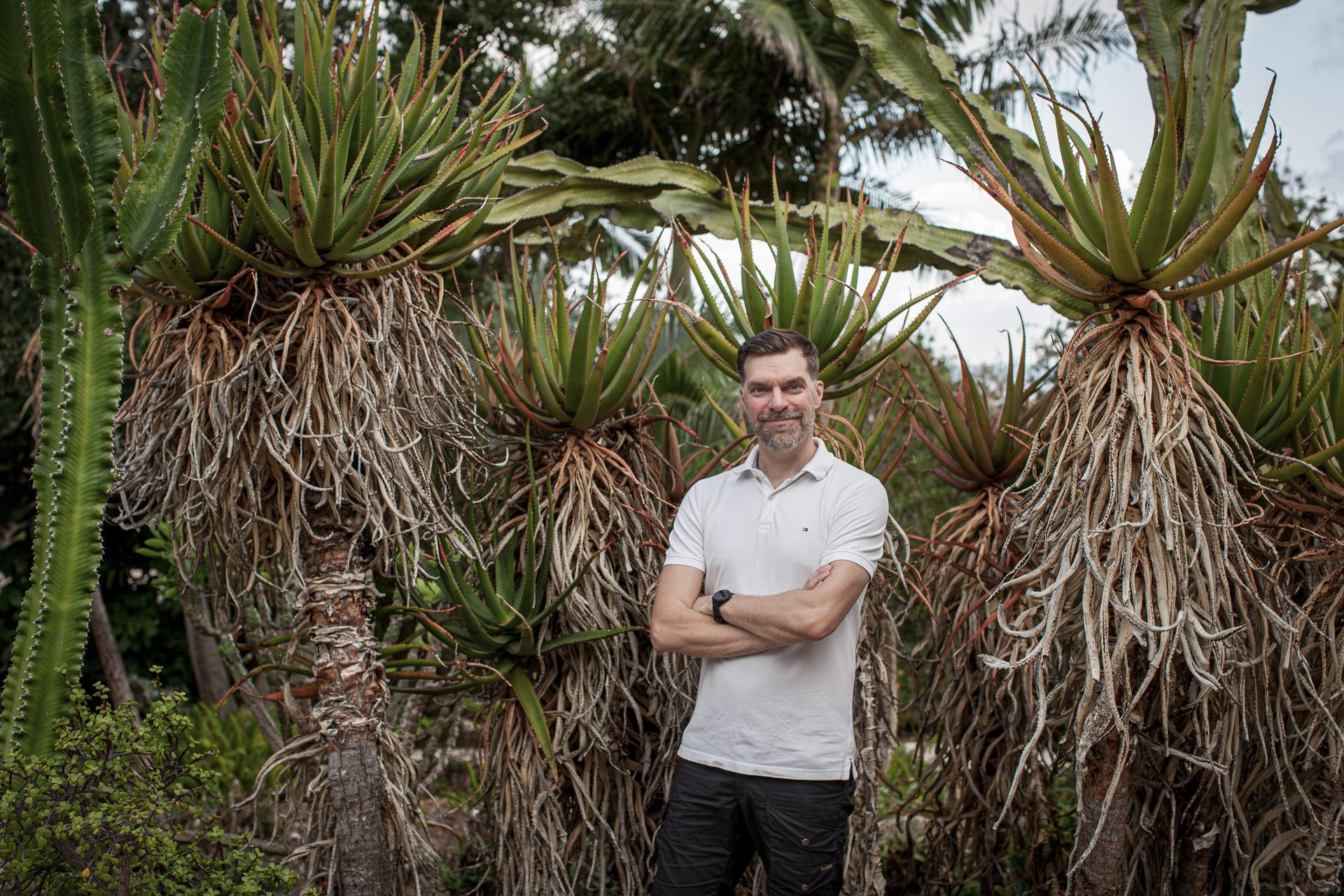Man stands in a lush botanical garden surrounded by tall aloe and cactus plants, Madeira lifestyle and natural greenery.