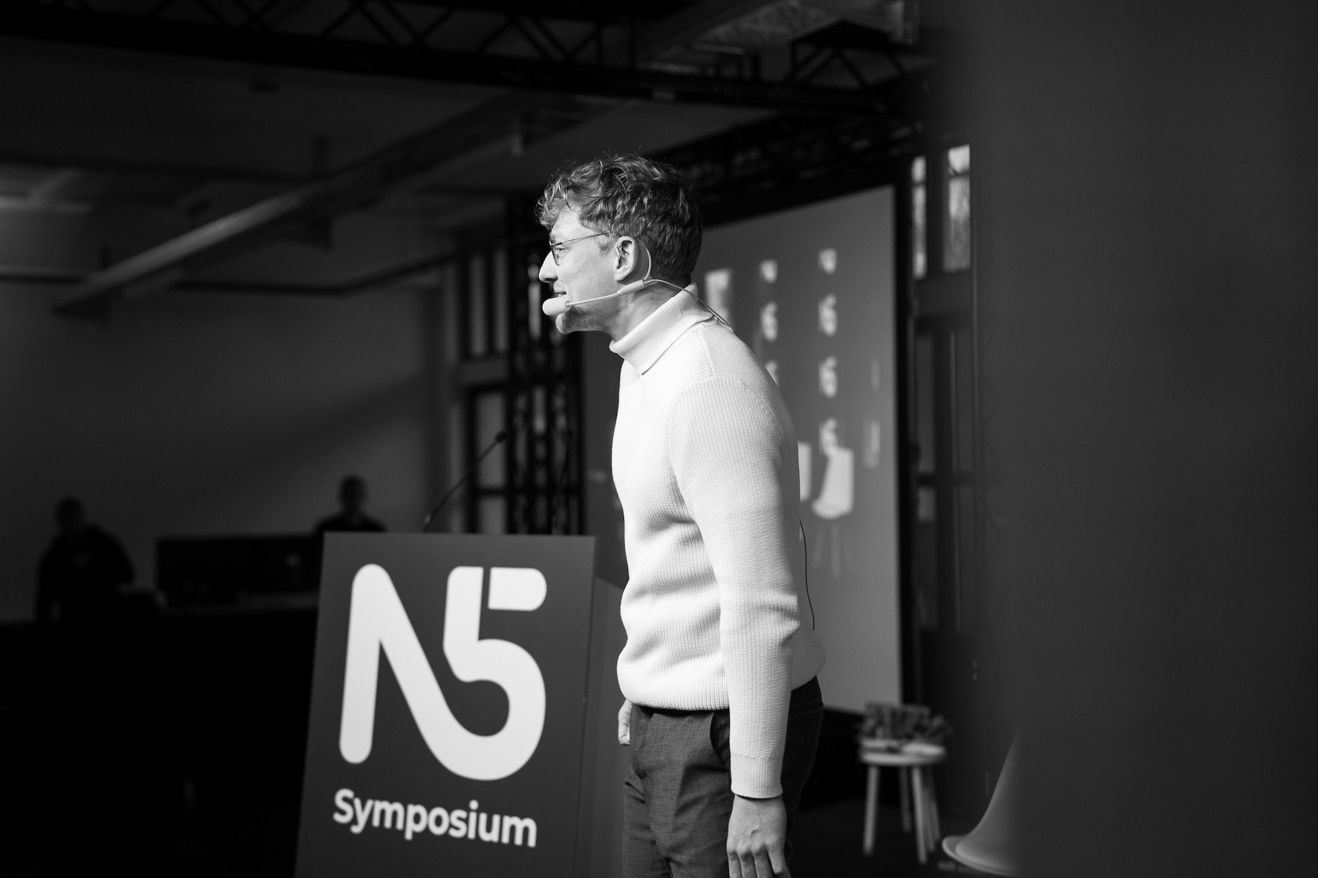 Moderator Przemek, Przemysław Żuk, steht auf einer Bühne und spricht lächelnd das Publikum an. Schwarz-weiß.