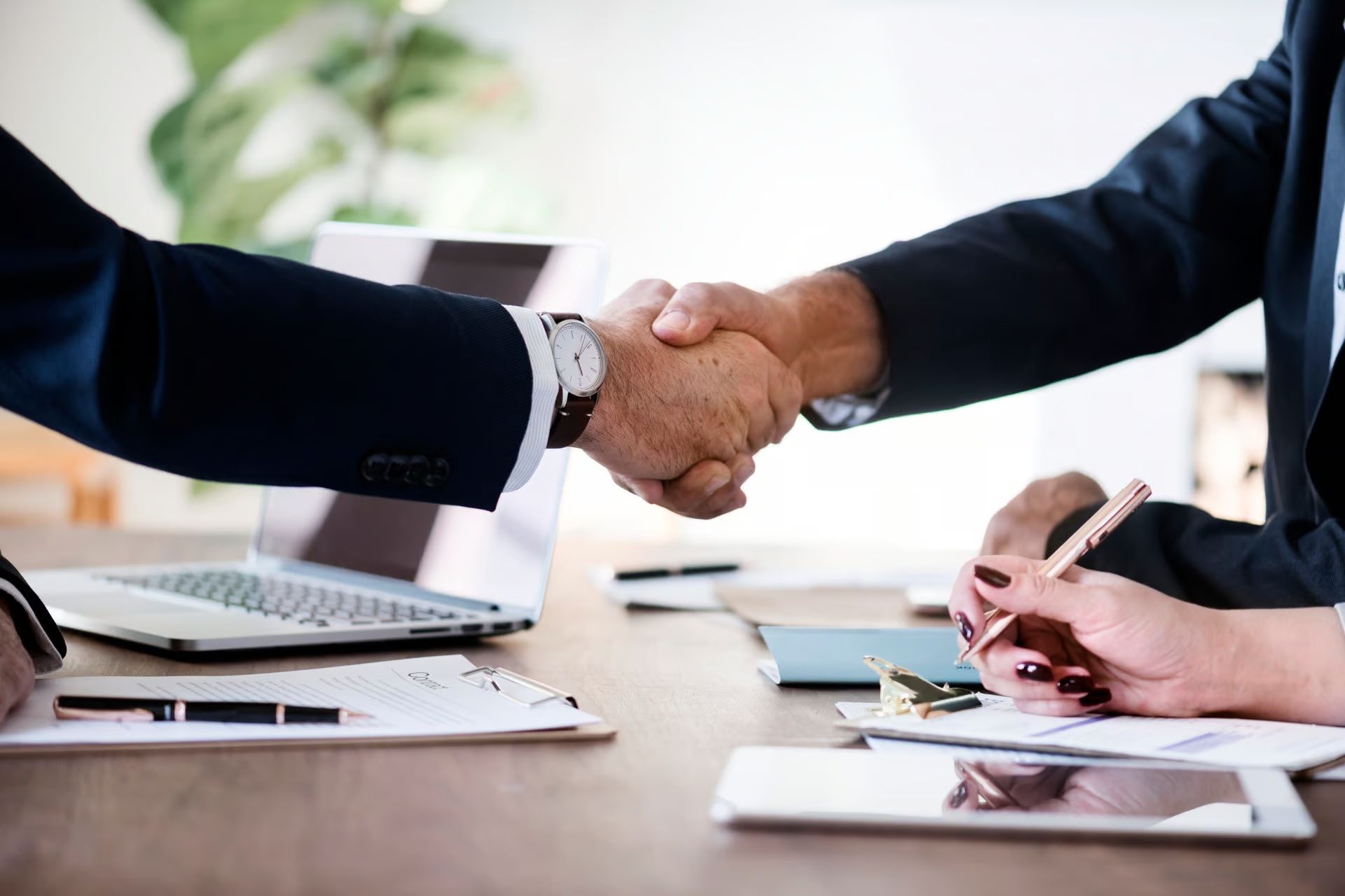 two people shaking hands over a desk with laptops