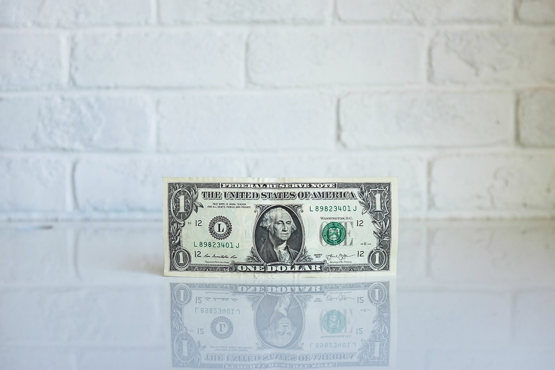 A dollar bill standing upright in front of a white brick wall
