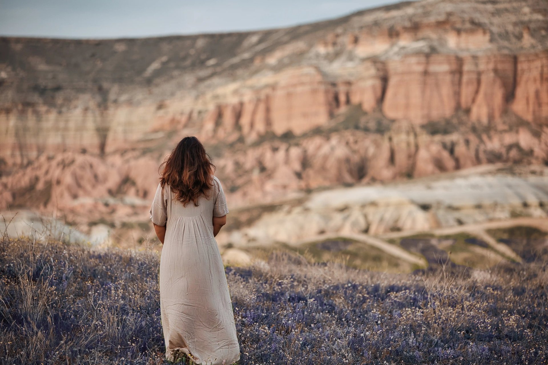 Woman in a beige dress standing in a lavender field with Cappadocia’s rock formations in the background