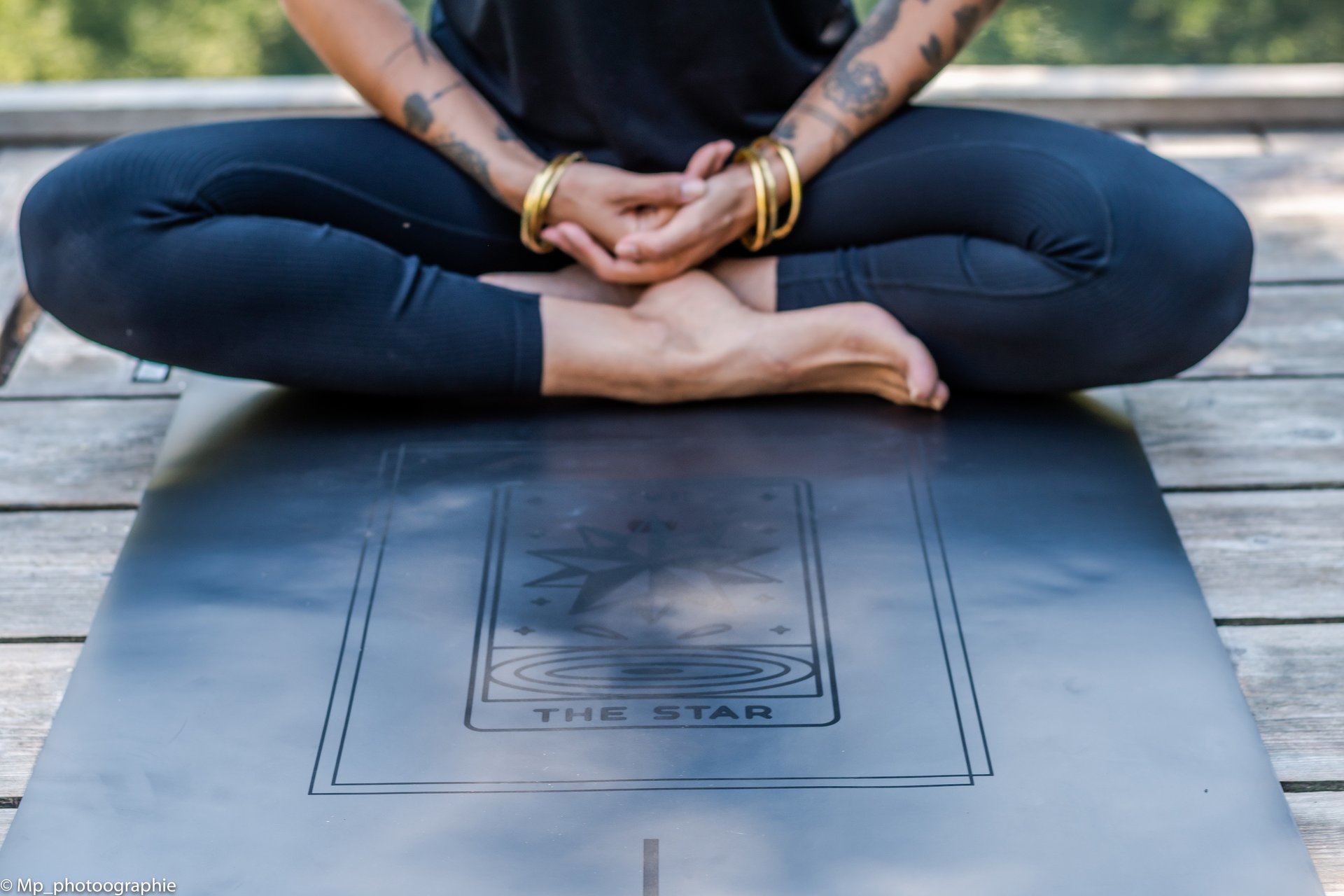 Tattooed woman sitting in a lotus pose on a black yoga mat featuring The Star tarot card design.