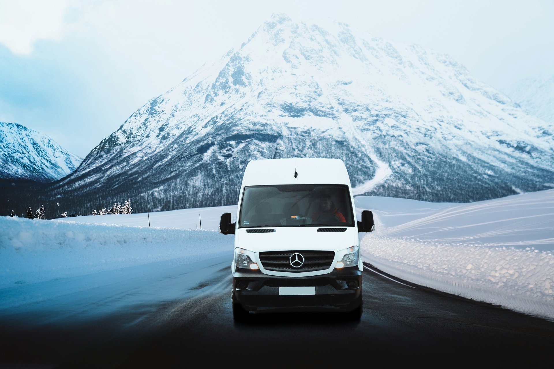 White Mercedes Sprinter van driving on a snowy mountain road in winter landscapes.
