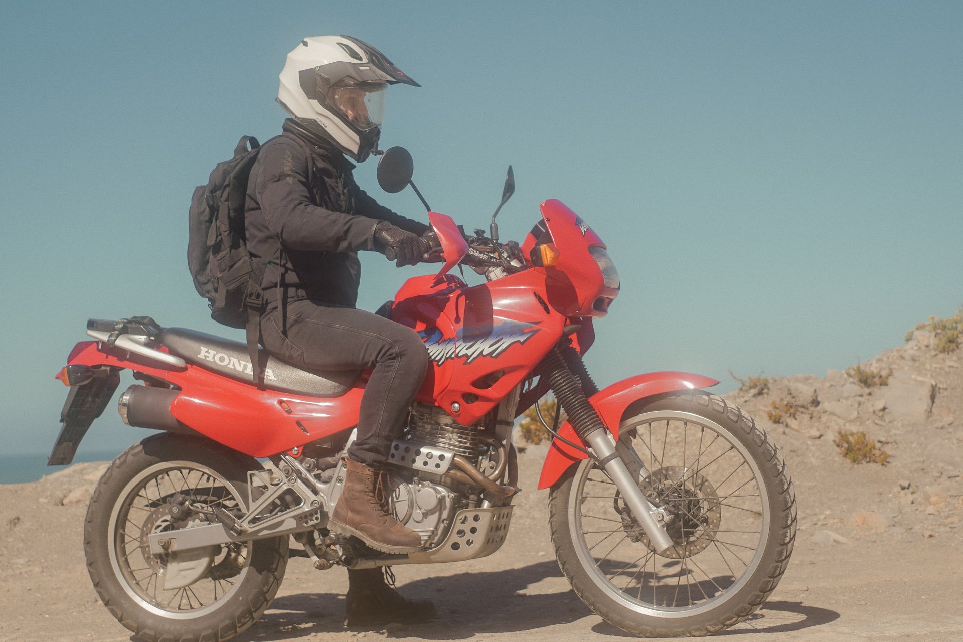 A man riding a Honda NX650 Dominator motorcycle out on a sandy surface