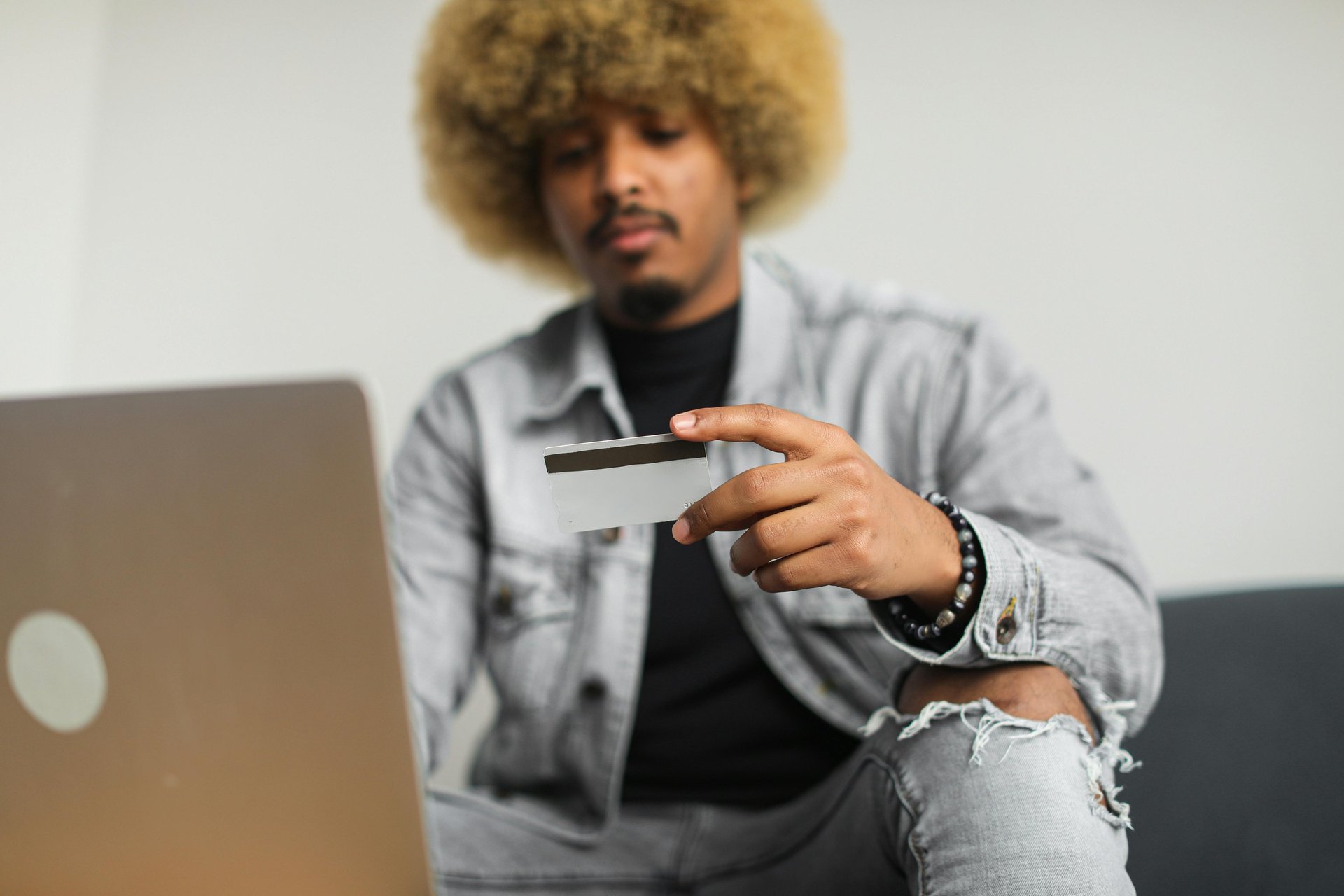 A man with an afro holds a credit card while using a laptop for secure online shopping and payments.