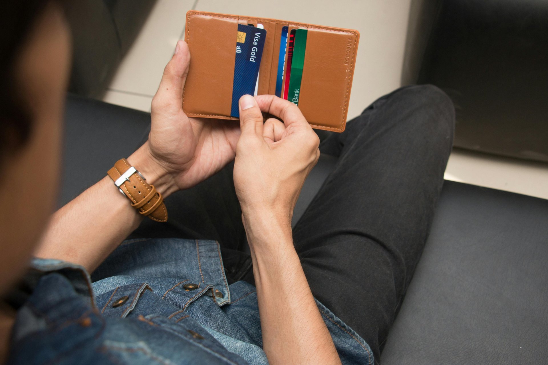 A man holding a slim brown leather bifold wallet with multiple credit cards and a Visa card.