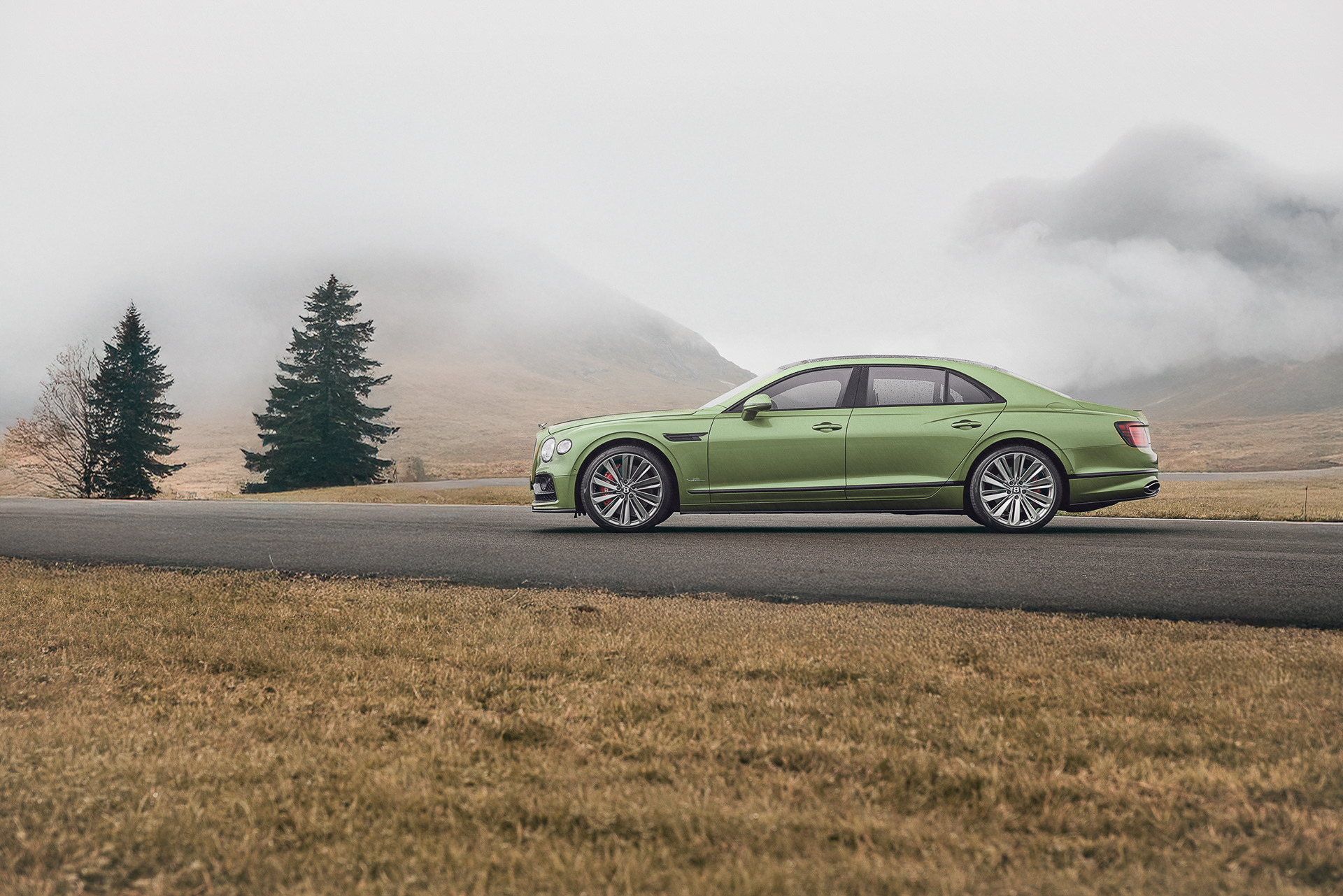 a green bentley driving down a road with a mountain in the background
