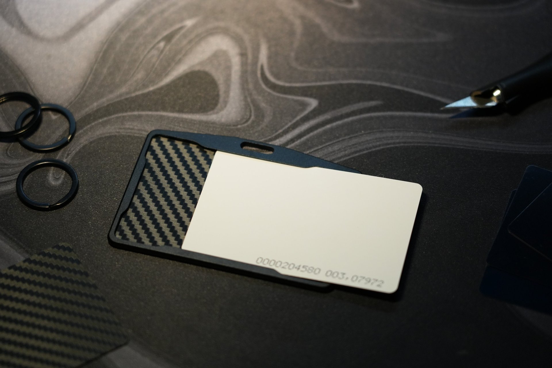 A minimalist carbon fiber ID card holder with a white proximity card on a black desk mat.