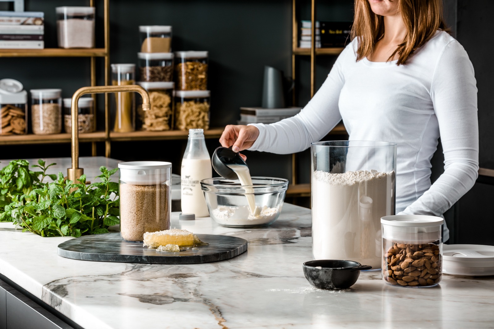Food product photography - a woman in a white shirt pouring milk in a bowl of flour