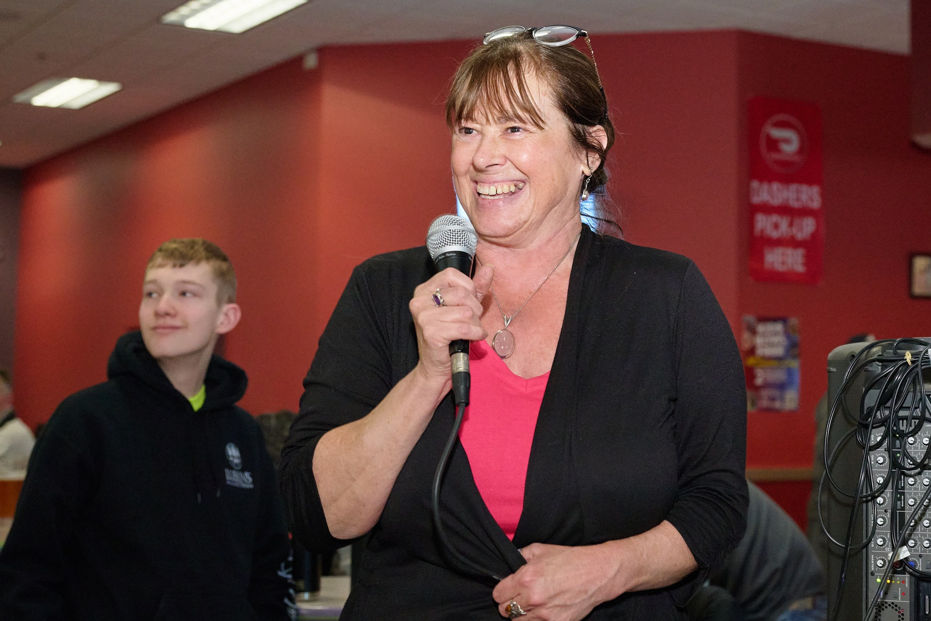 a woman in a black jacket is holding a microphone and smiling