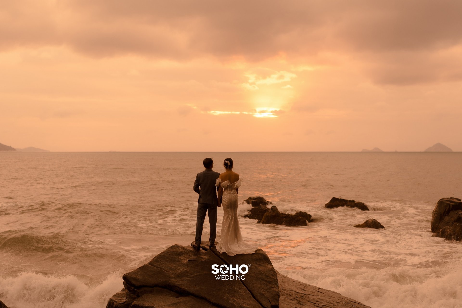 a couple standing on a rock in front of a sunset