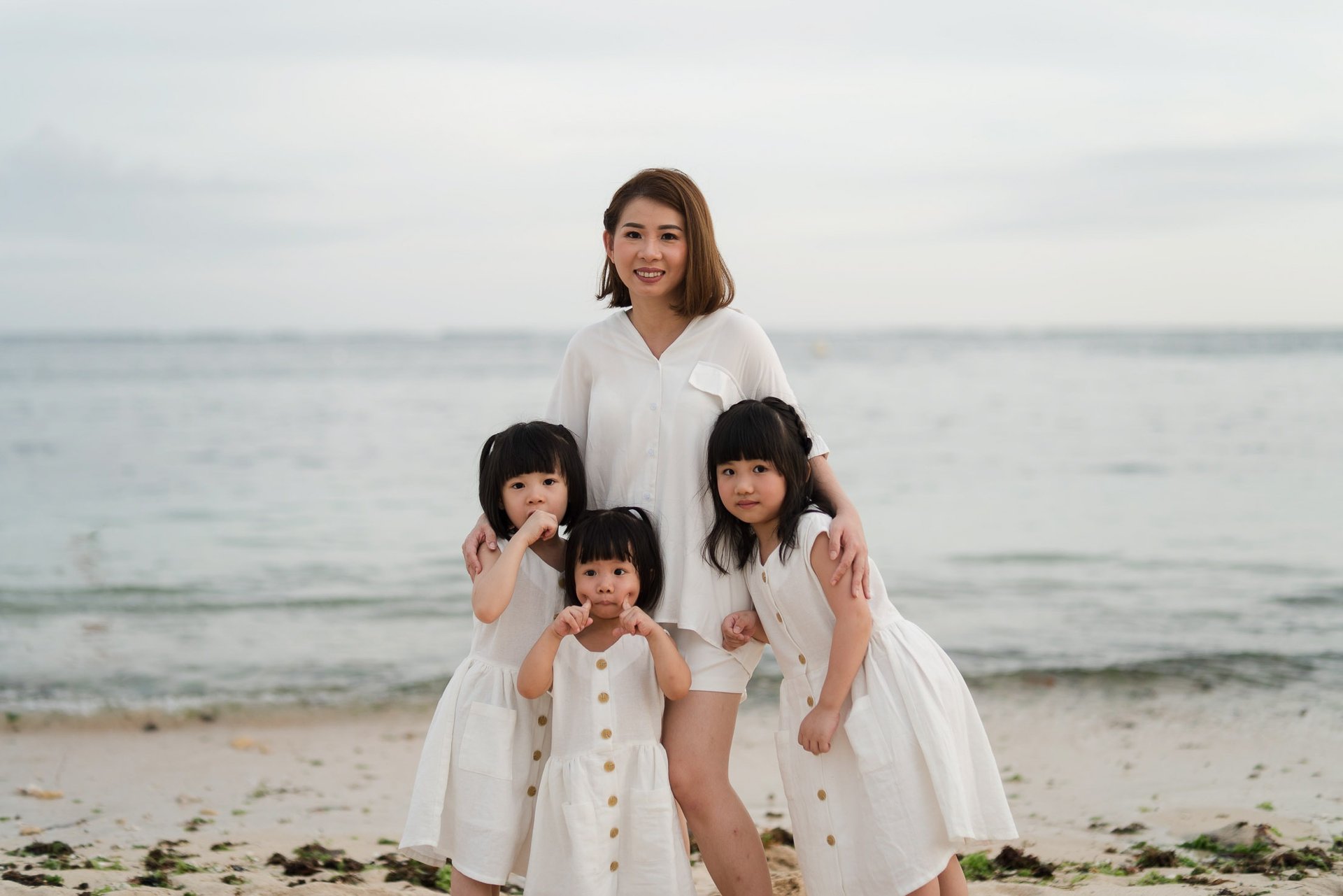 Mother and daughters standing together by the ocean during a family photography session at The Mulia Nusa Dua Bali