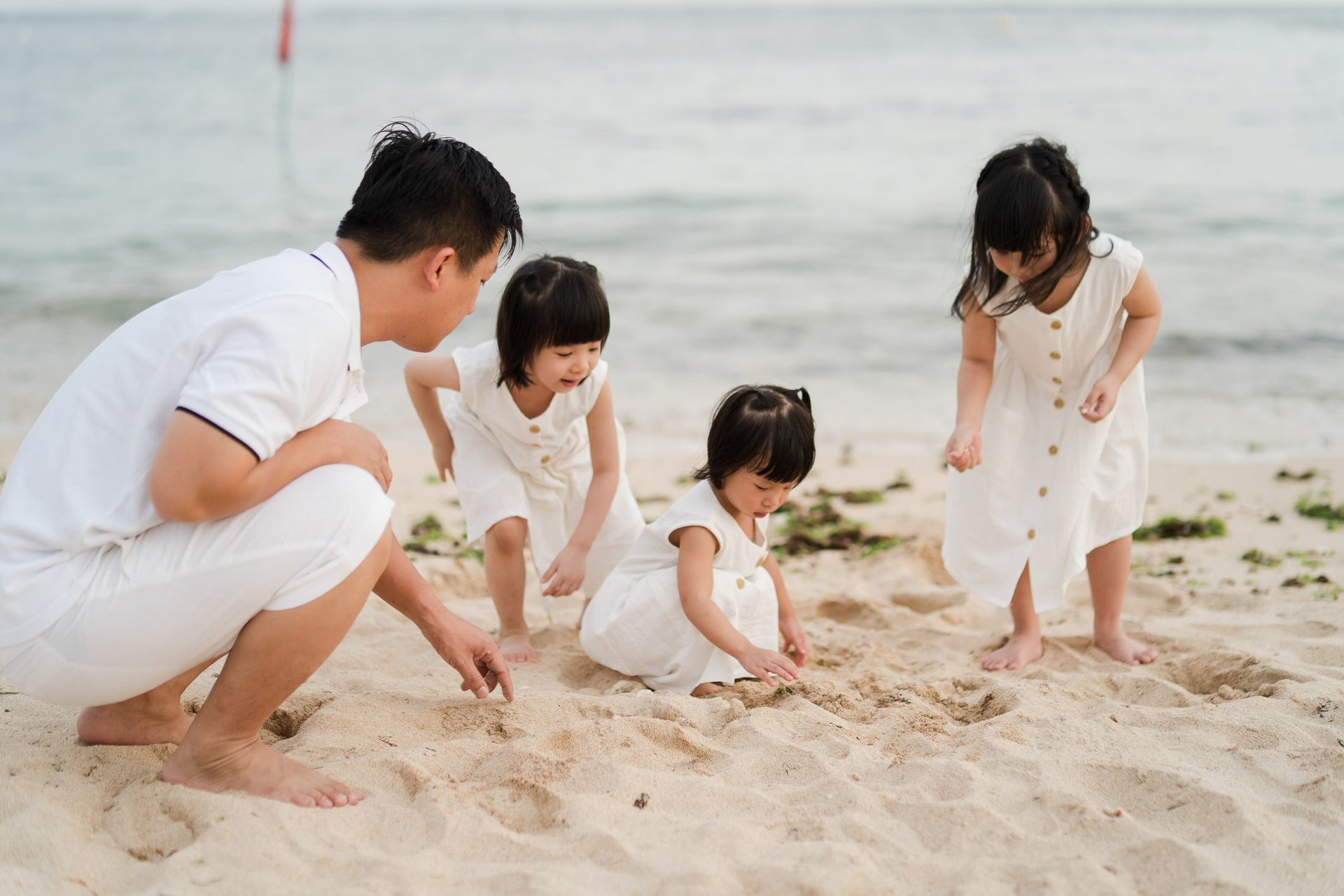 Father and children playing with sand on the beach at The Mulia Nusa Dua Bali during a relaxed family photo session