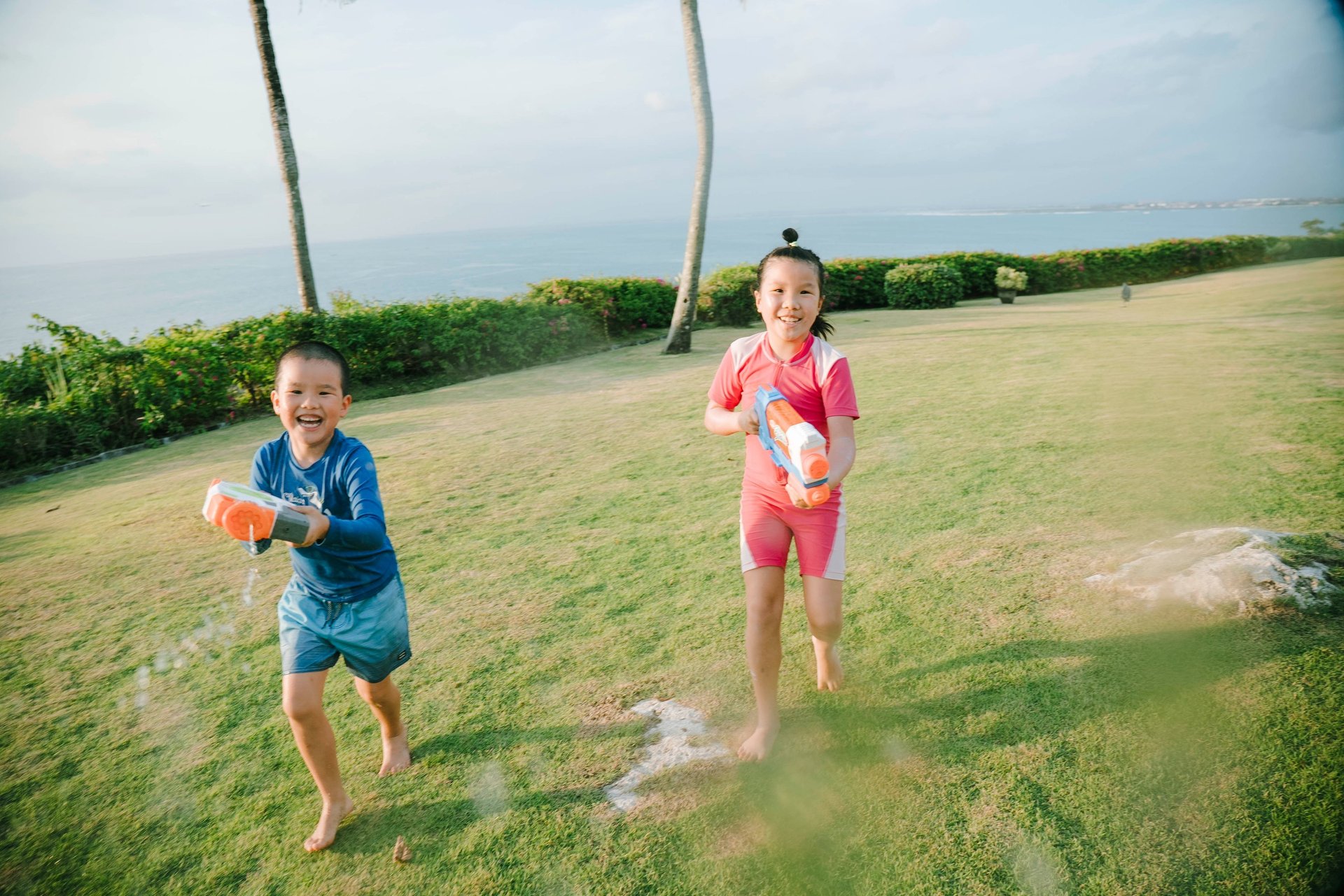 two Children playing with water guns during a family photography session at AYANA Villas Jimbaran Bali
