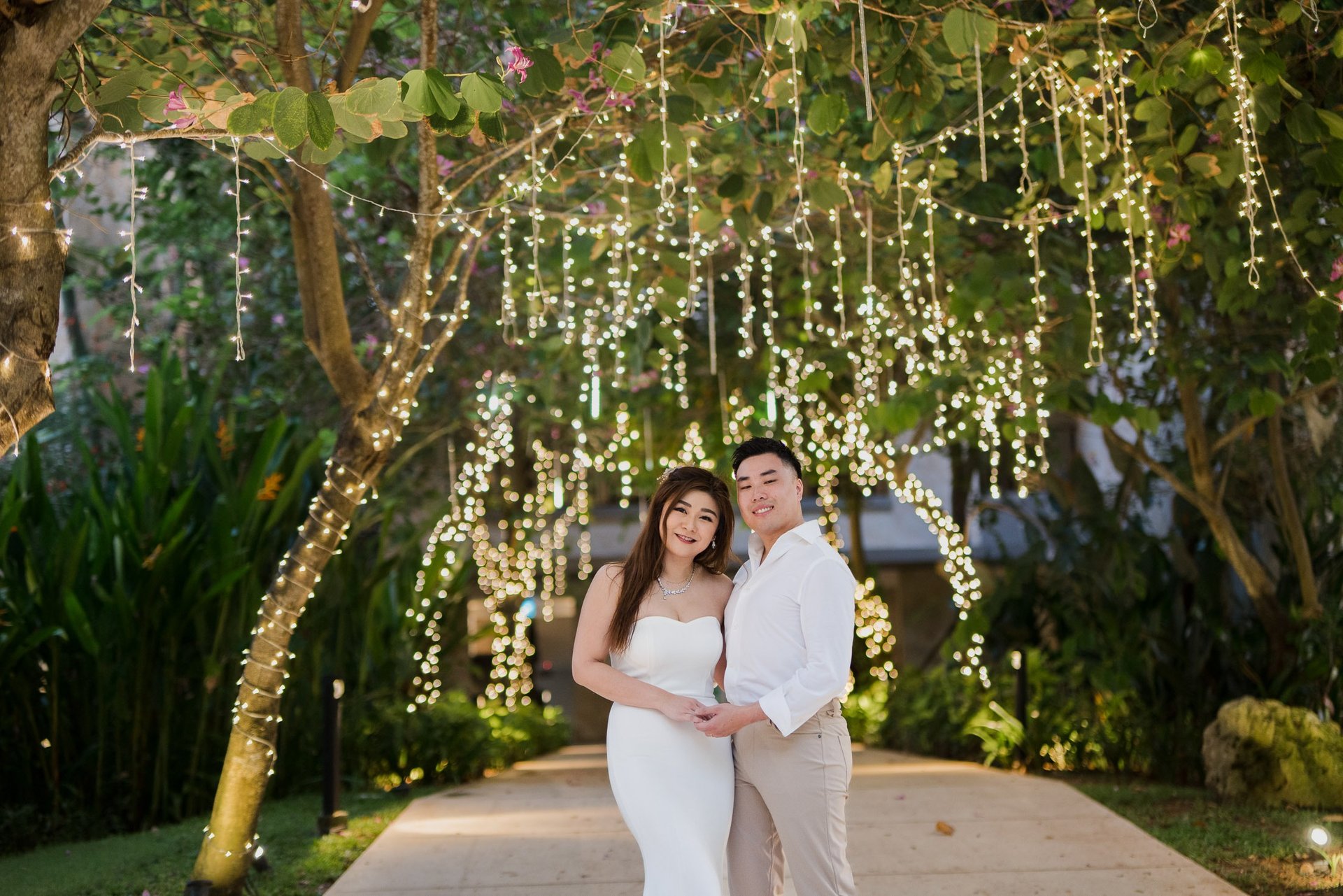 Couple standing under hanging garden lights during a romantic evening prewedding session at Apurva Kempinski Bali