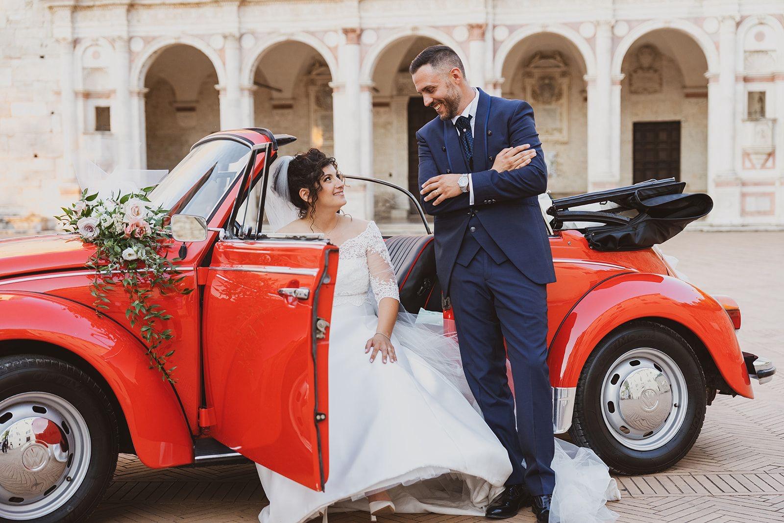 Sposi sorridenti a bordo del maggiolone rosso addobbato per il loro matrimonio
