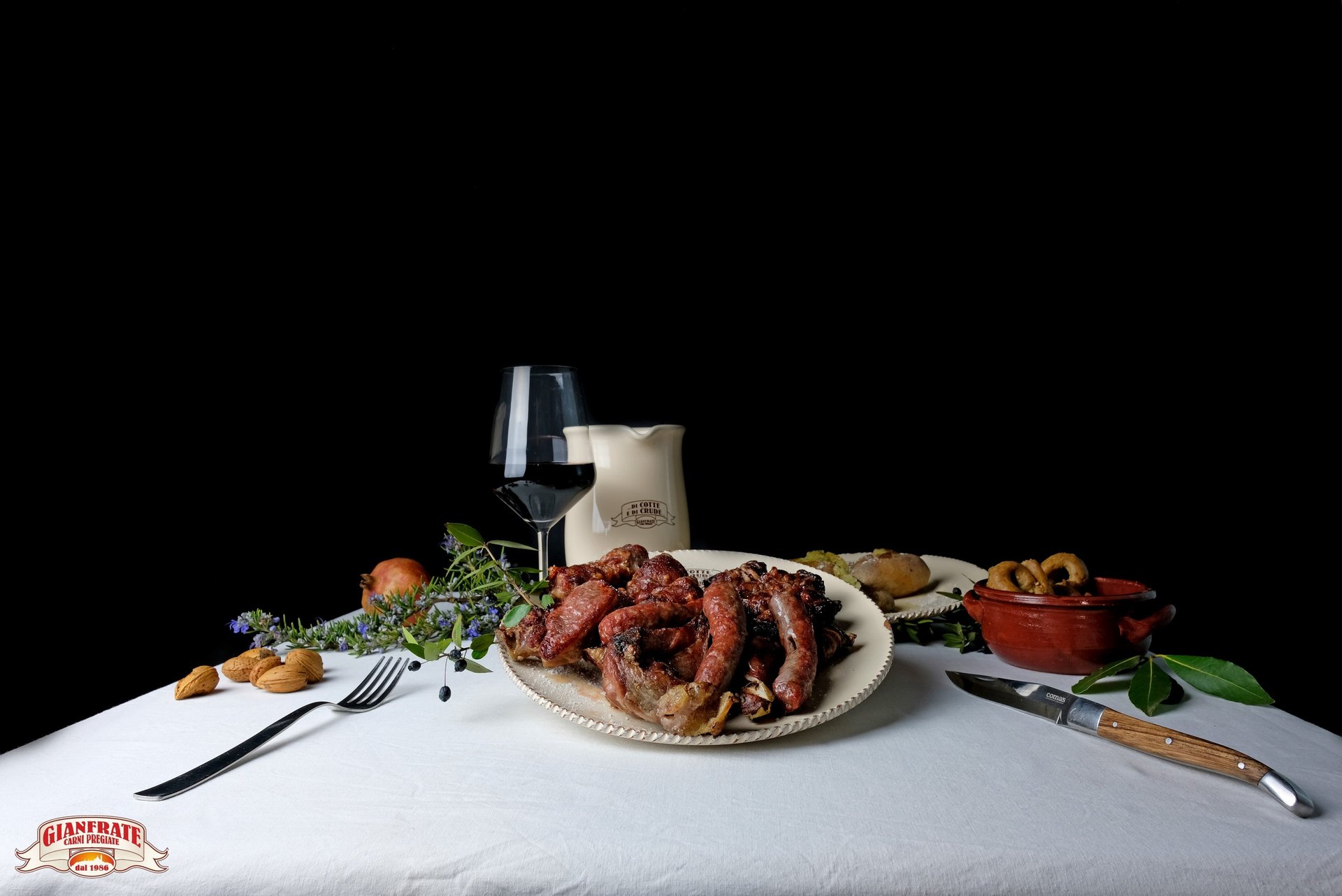 Traditional Italian dinner featuring grilled sausages, red wine, and savory sides on a white tablecloth.