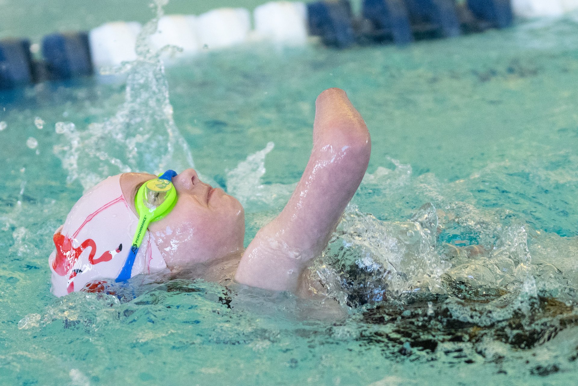 Young girl swimming on her back in pink swim cap with flamingos and blue and green goggles
