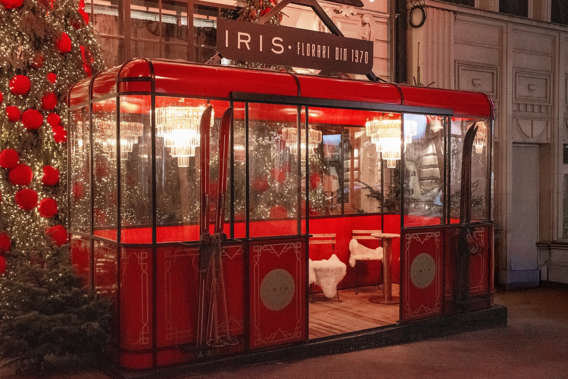 A red vintage ski gondola decorated for Christmas with chandeliers and cozy seating inside.