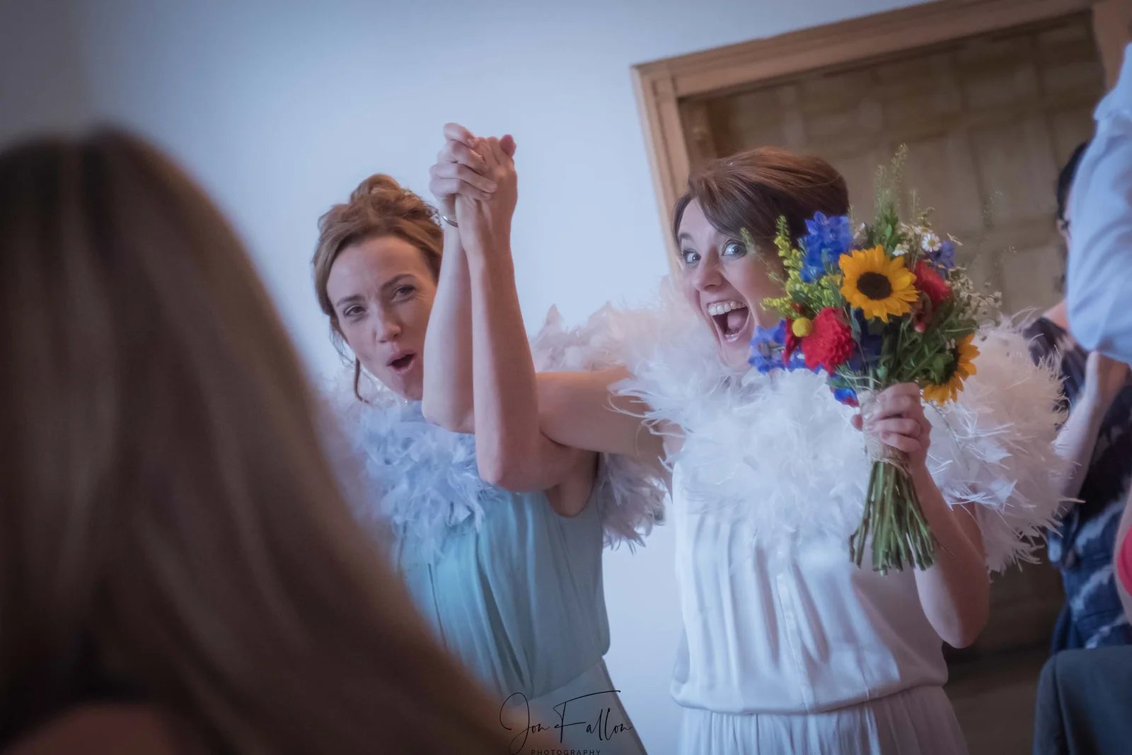 Two brides wearing white feather boas celebrate at a wedding reception.