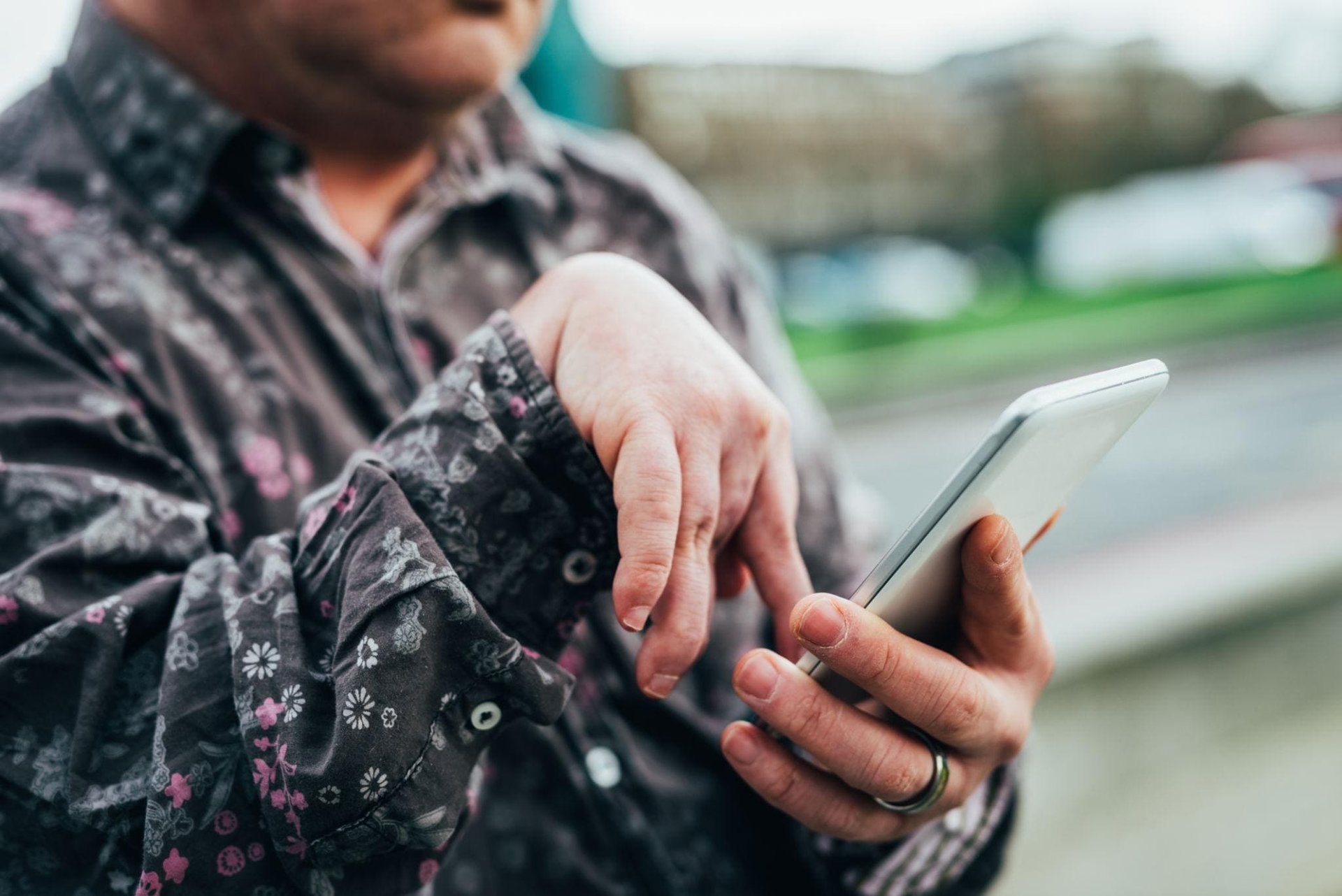 A person in a patterned shirt uses a smartphone outdoors