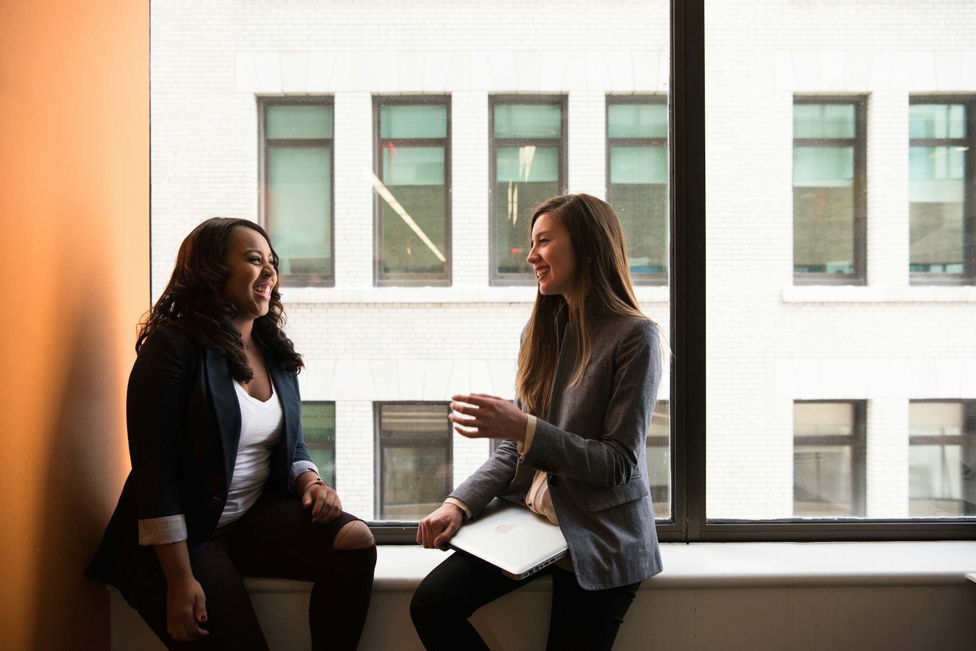 Two diverse female professionals discussing business strategy during a meeting by an office window.