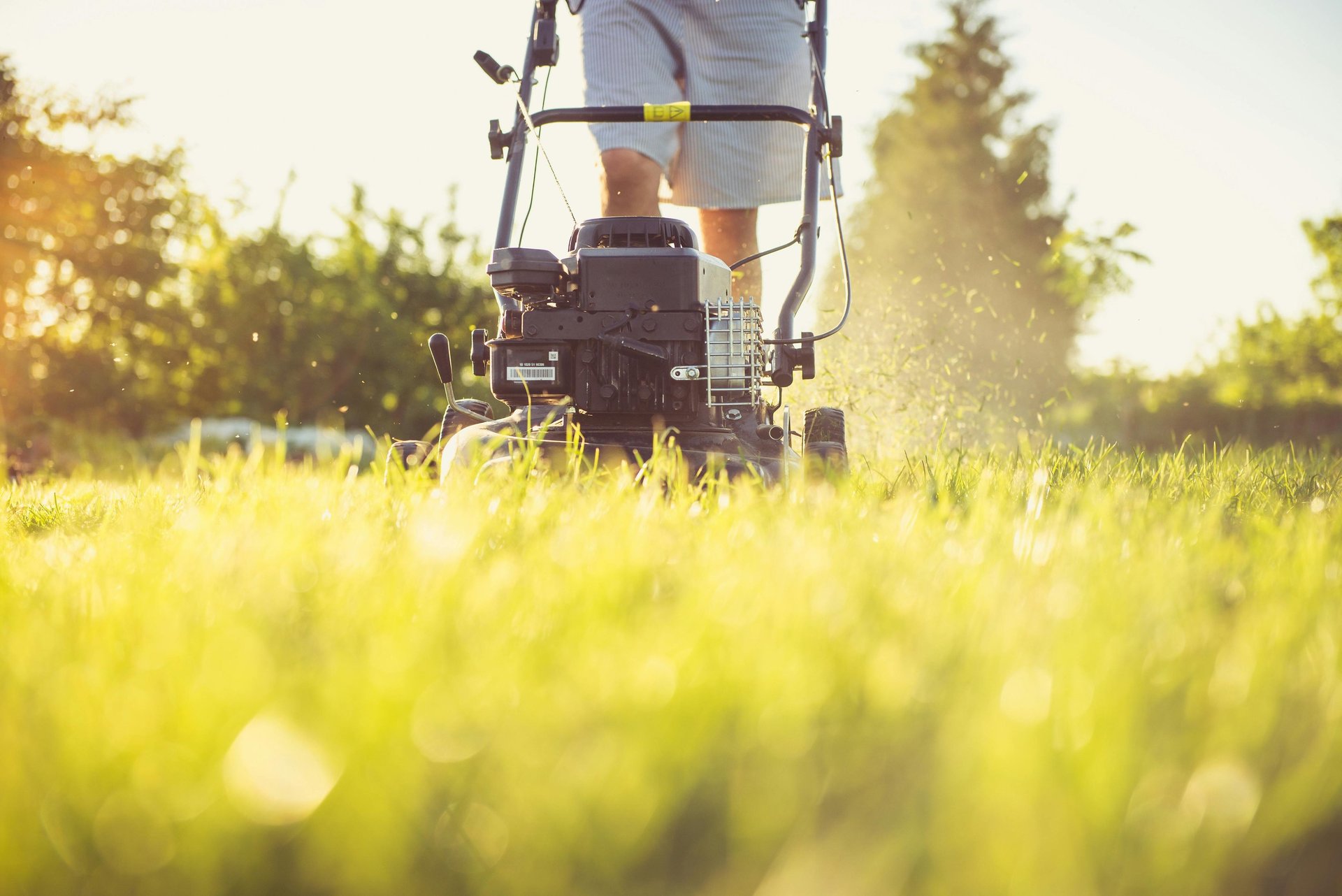 a man is standing in the grass with a lawn mower, person mowing the lawn