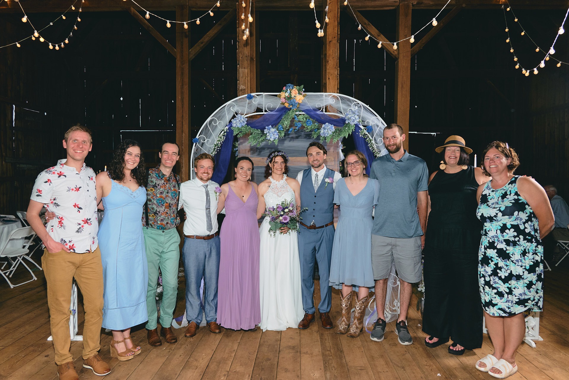 a group of people including a bride and groom standing in front of a wedding arch