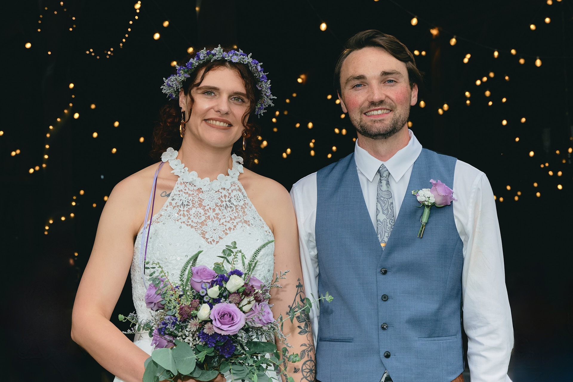 a bride holding a bouquet standing next to the groom with lights behind