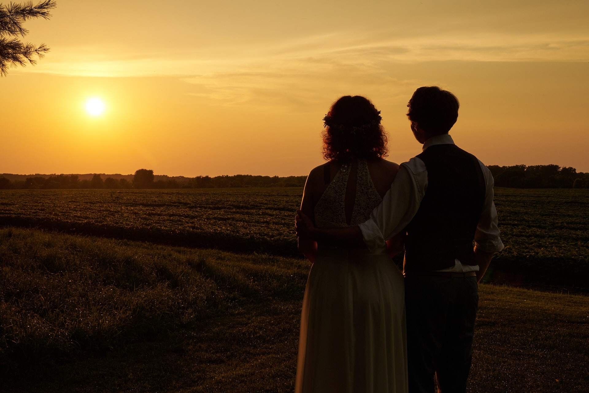a bride and a groom looking at the sunset in a farm land