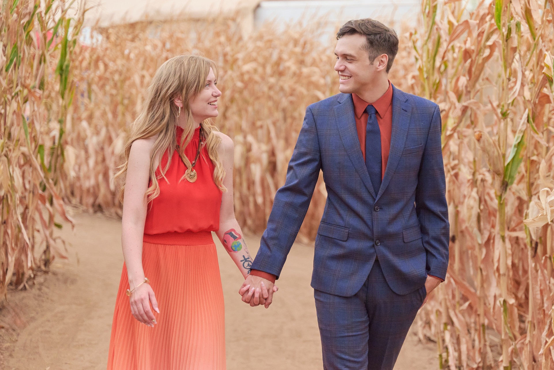 a man and woman holding hands and walking through a corn maze