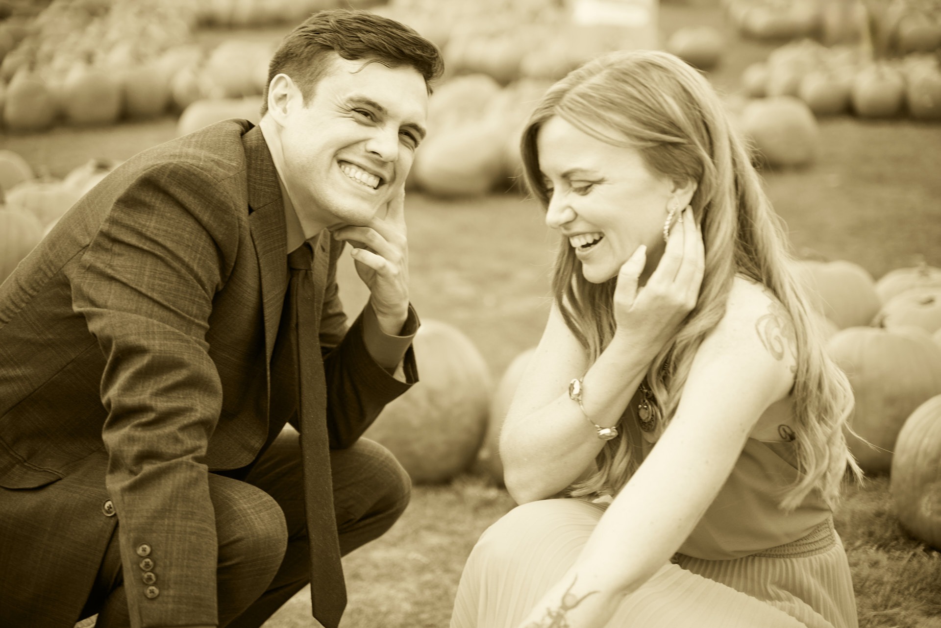 a man and woman in a field of pumpkins smiling in sepia style