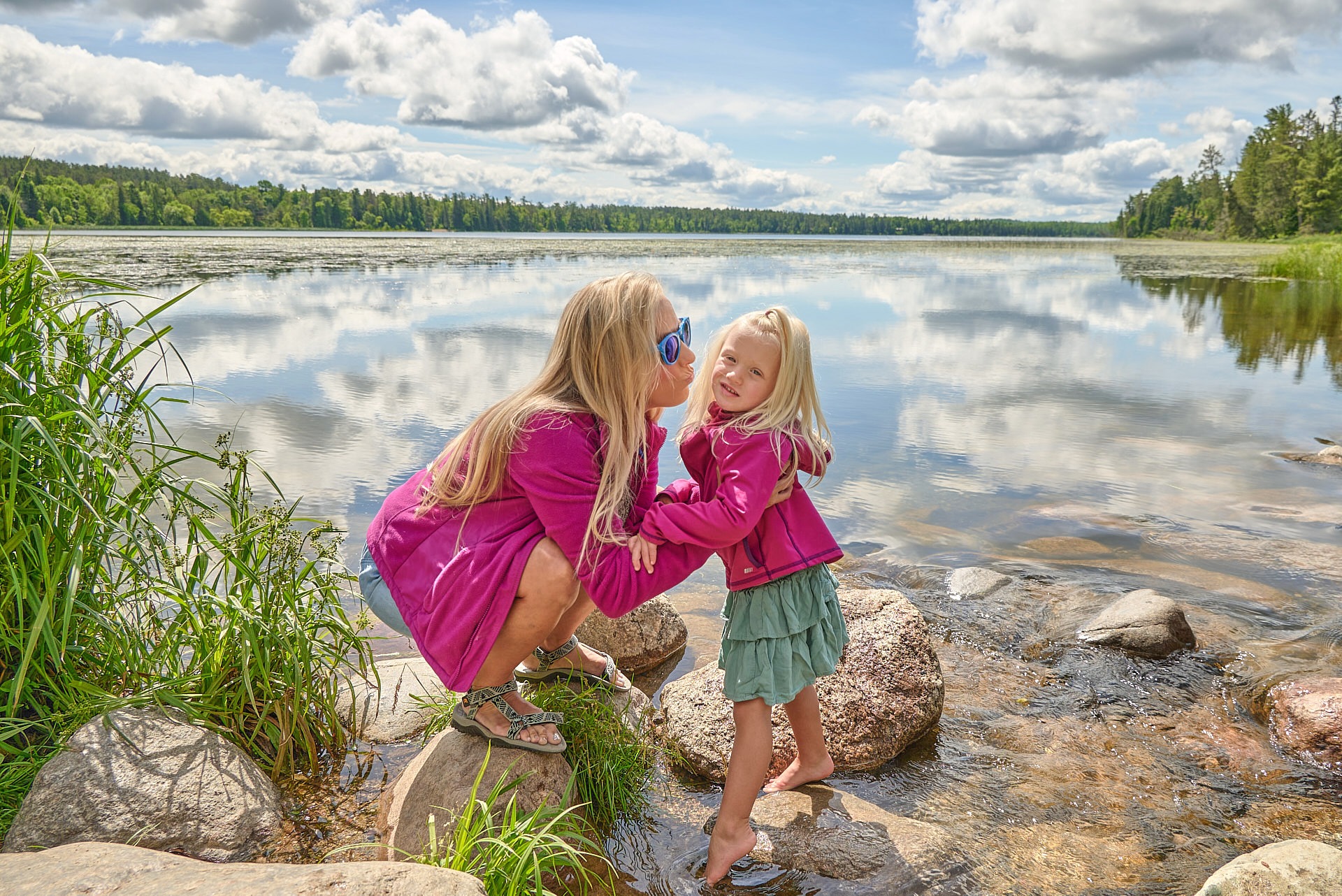 a mother and her girl in pink jackets standing in front of a lake