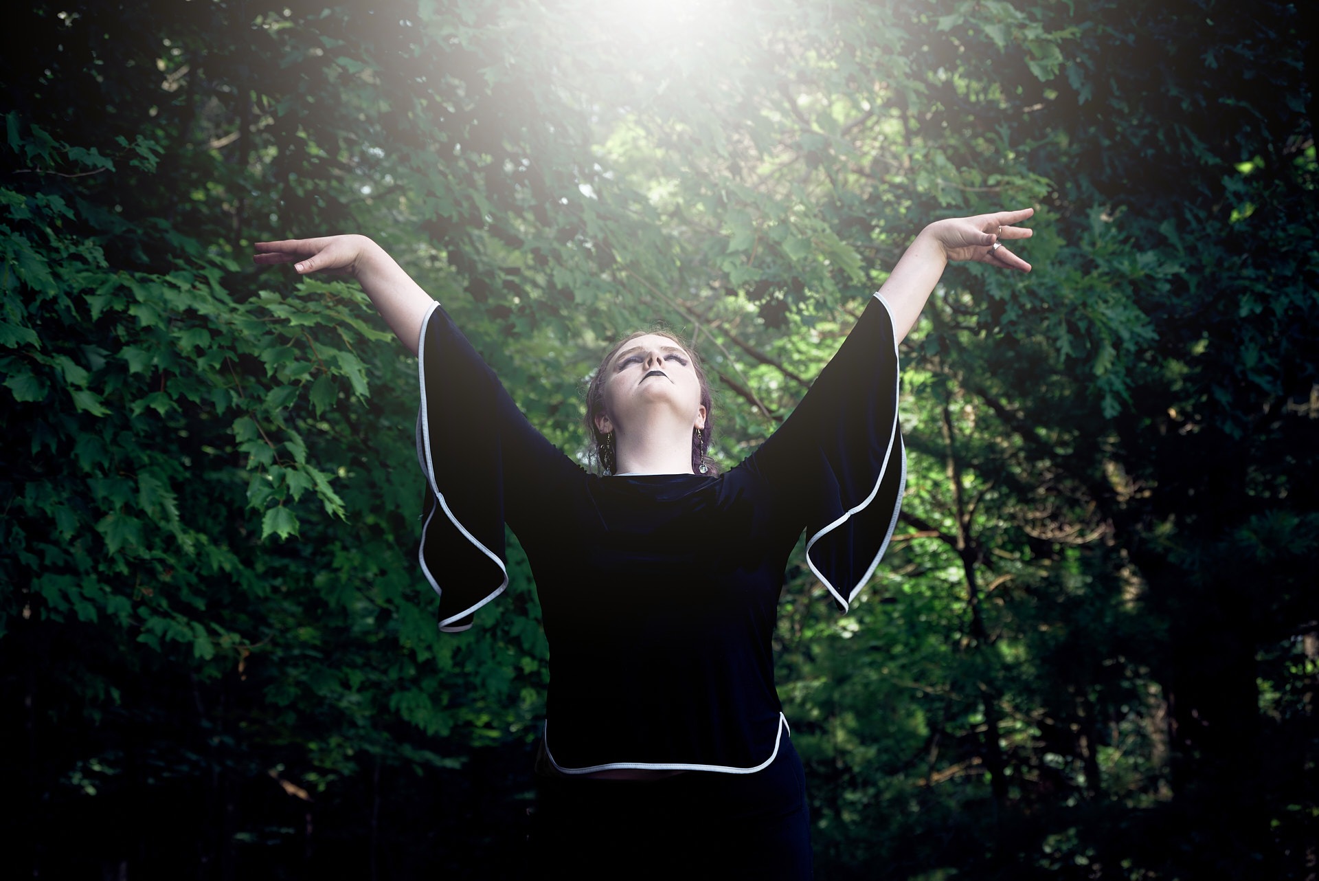 a woman with her arms outstretched up and she is looking up to the sun in the forest