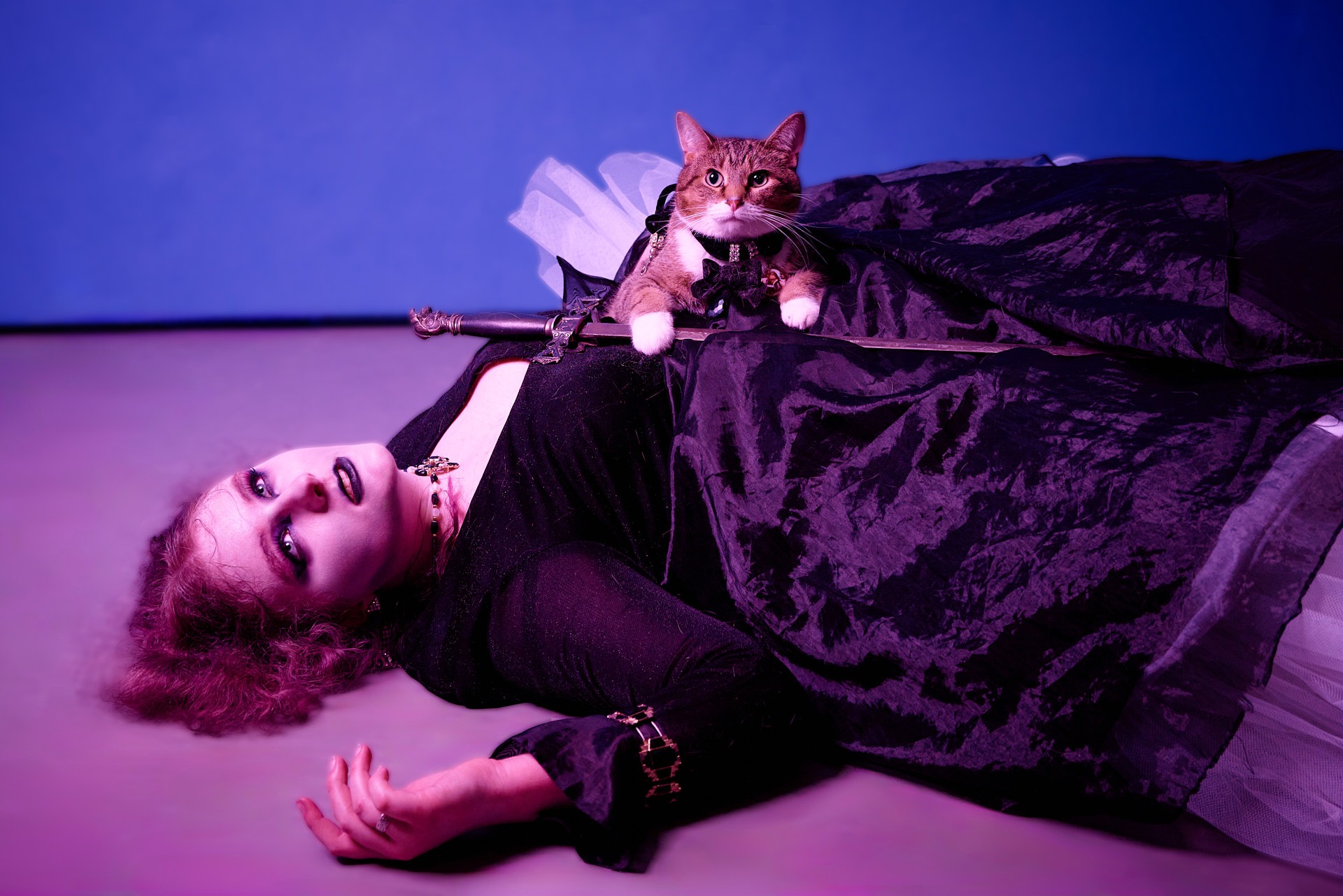 a girl in a black dress dying on the ground with a cat holding a sword on top of her body
