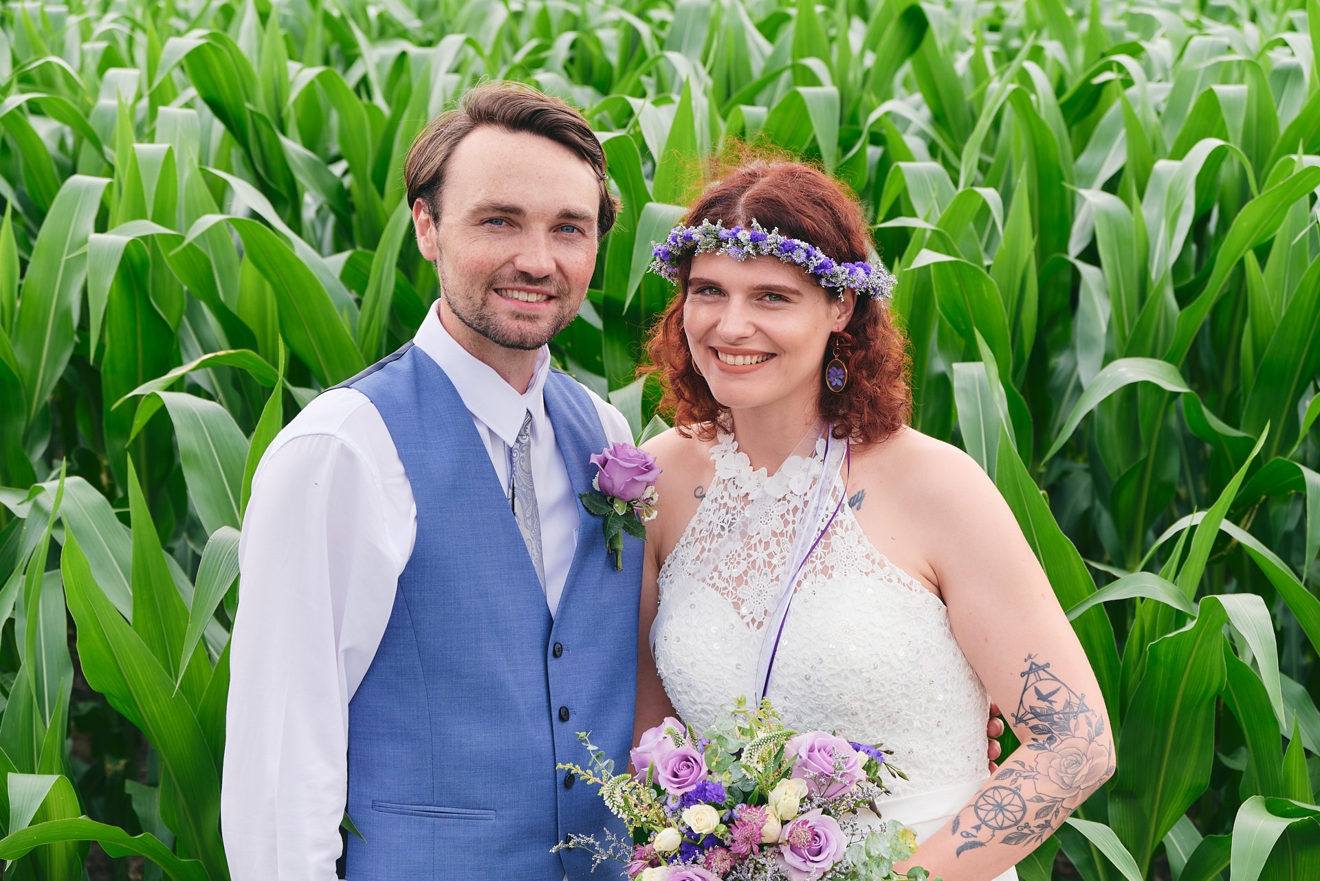 a bride holding a bouquet and a groom standing next to each other in a corn field
